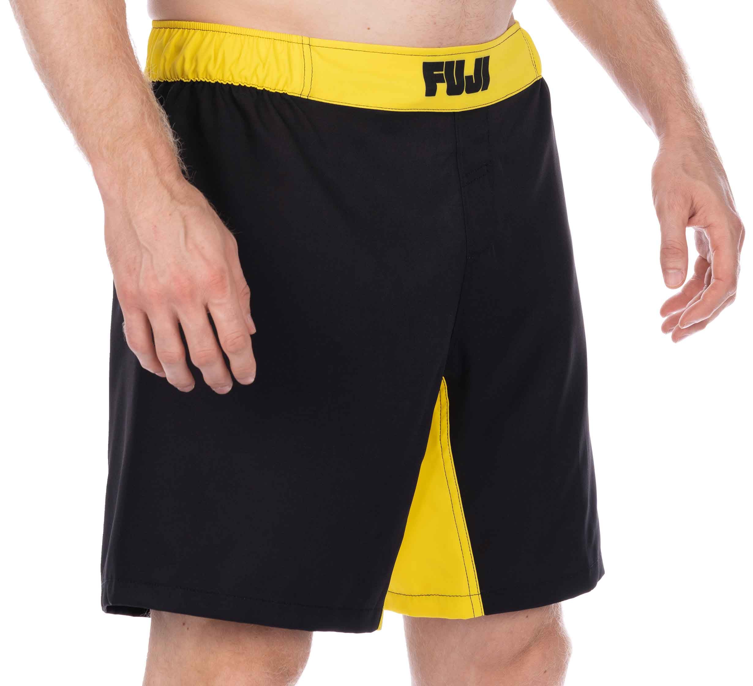 Someone is wearing the Essential Grappling Yellow Fight Shorts, featuring black fabric with a yellow waistband, yellow front detailing, and "FUJI" printed on the waistband. Only the lower torso and arms are visible.