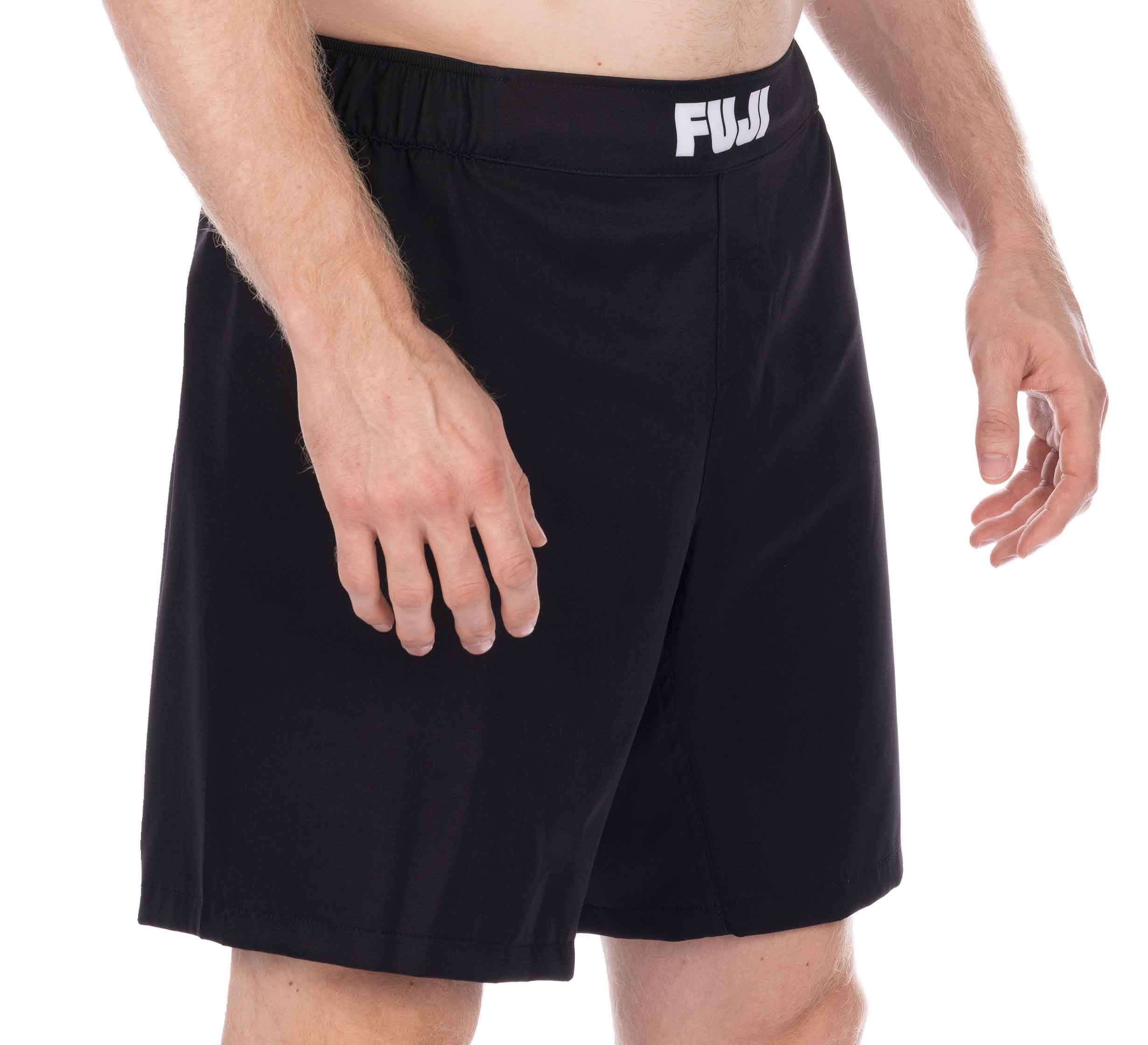 A person models the Essential Grappling Black Fight Shorts, featuring a white "FUJI" logo on the waistband, shown from waist to mid-thigh with arms relaxed at their sides against a plain white background.