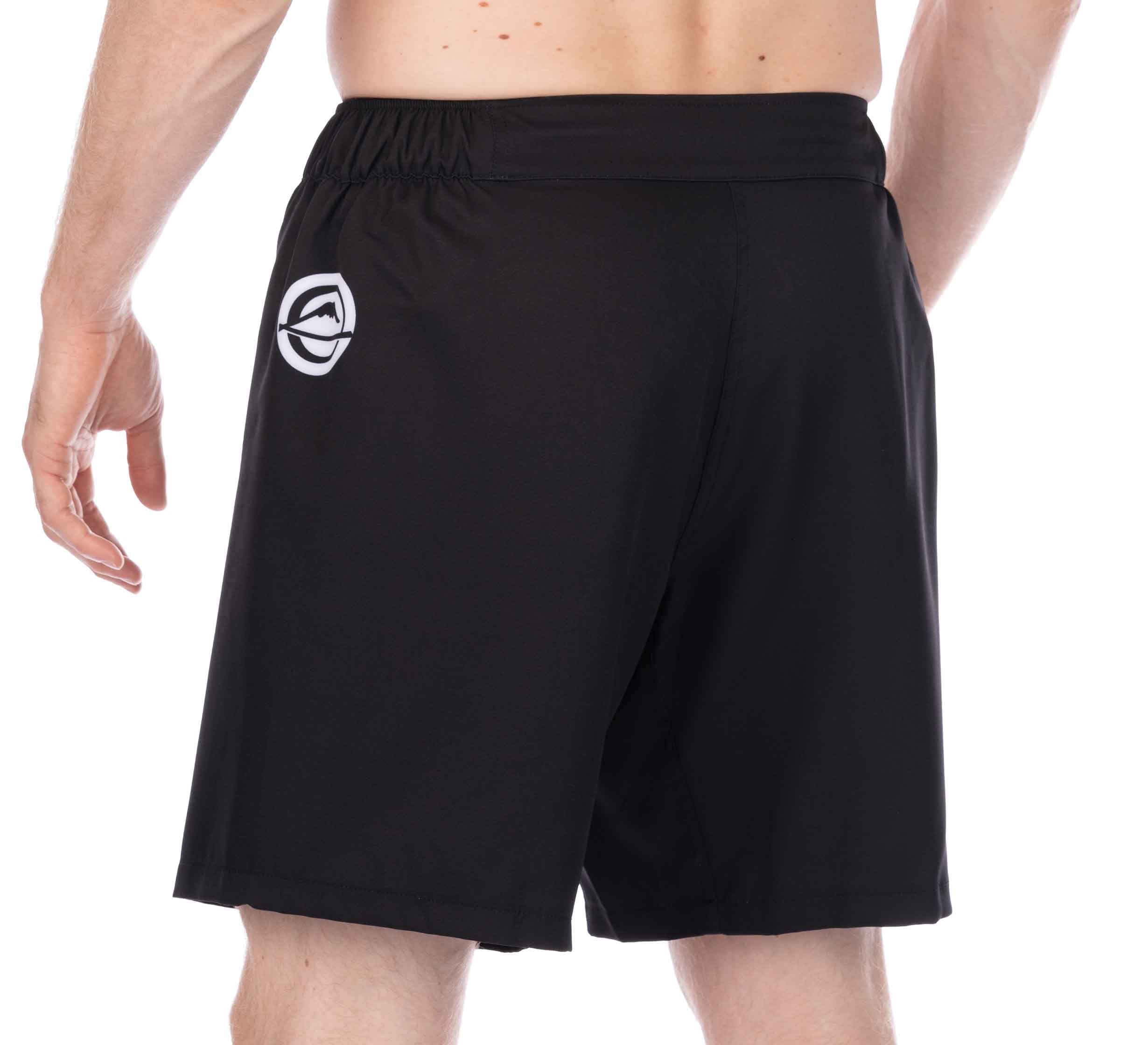 A person is shown from the waist down, facing away, wearing Essential Grappling Black Fight Shorts with an elastic waistband and a small white logo on the upper left back.