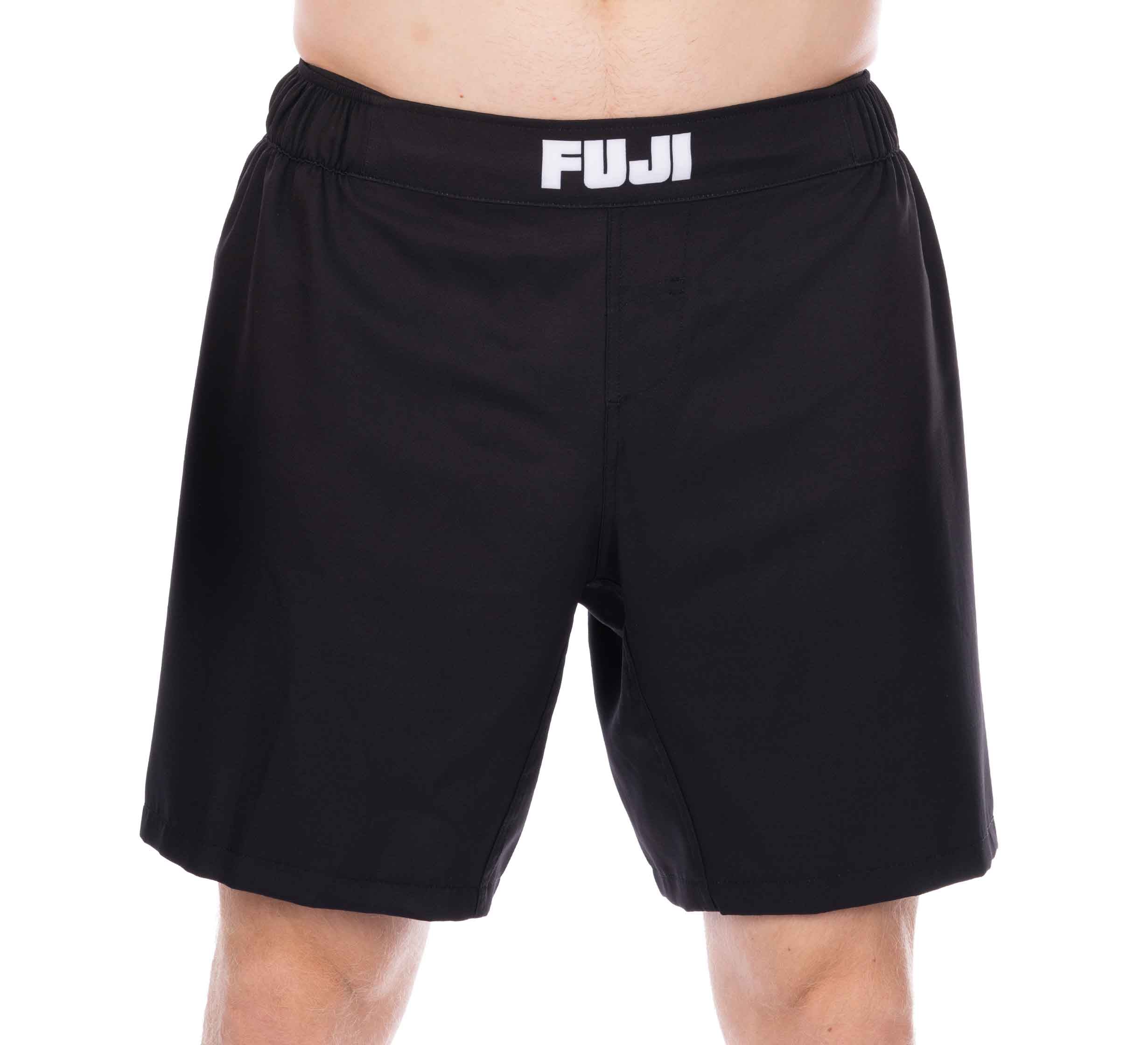 A person wearing Essential Grappling Black Fight Shorts with "FUJI" in white on the waistband. The image focuses on the shorts, showing part of the legs and torso.