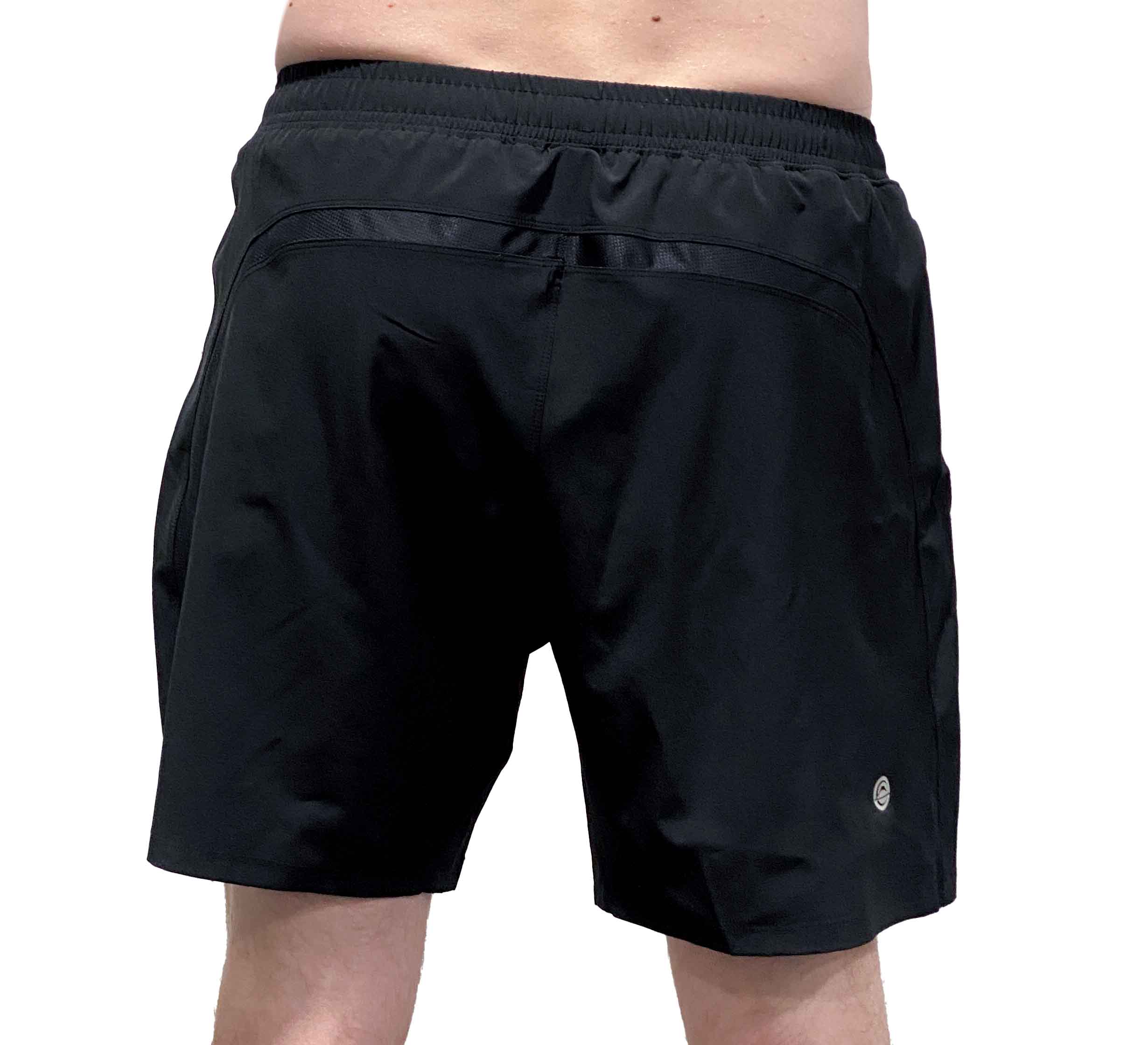 A person wears Commuter Workout Shorts in black, featuring an elastic waistband and a small circular logo on the lower left leg. Only their lower torso and upper legs are visible as they stand facing away from the camera.