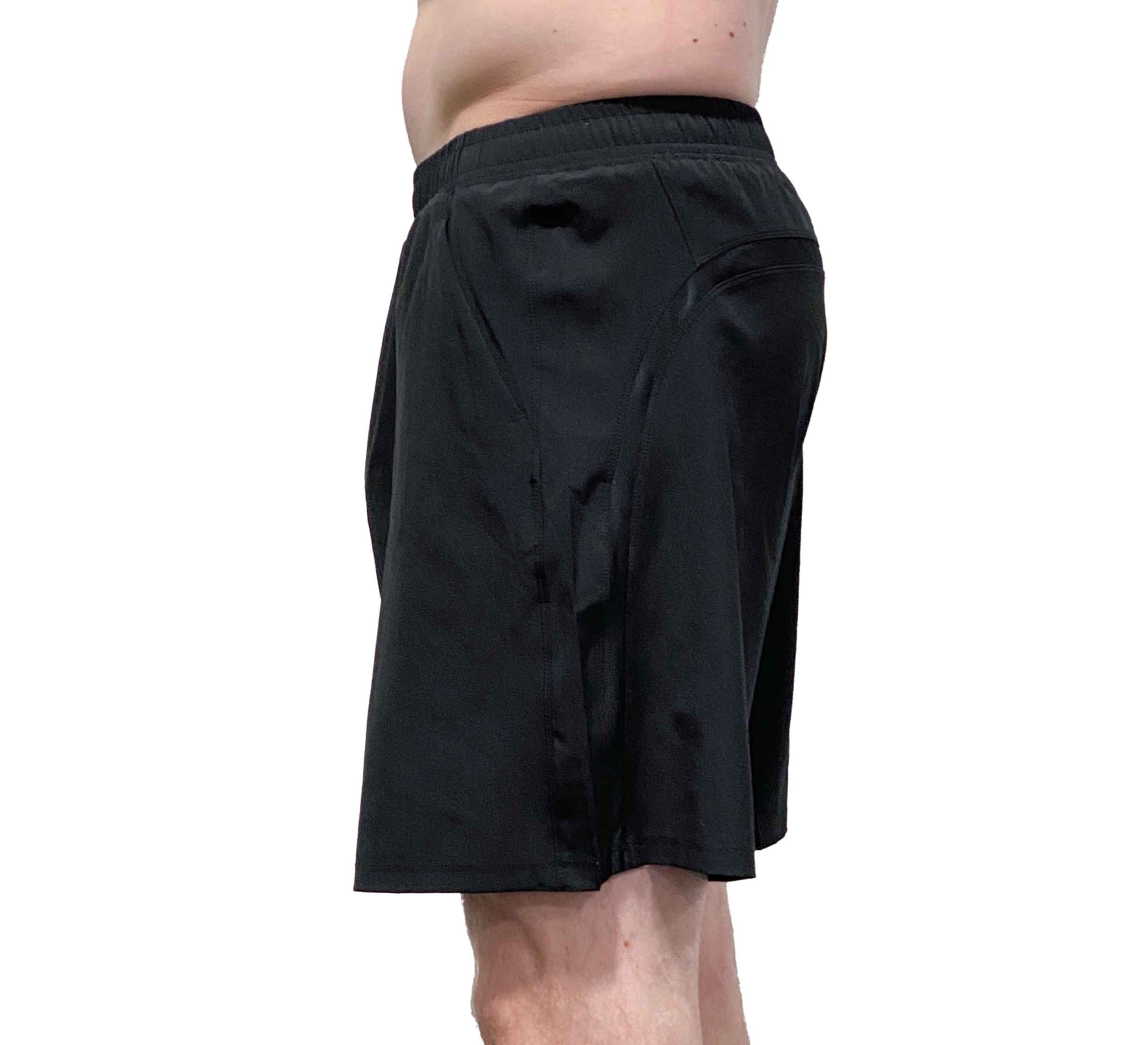 A person models the Commuter Workout Shorts in black, standing in profile against a white background to display the side view and elastic waistband.