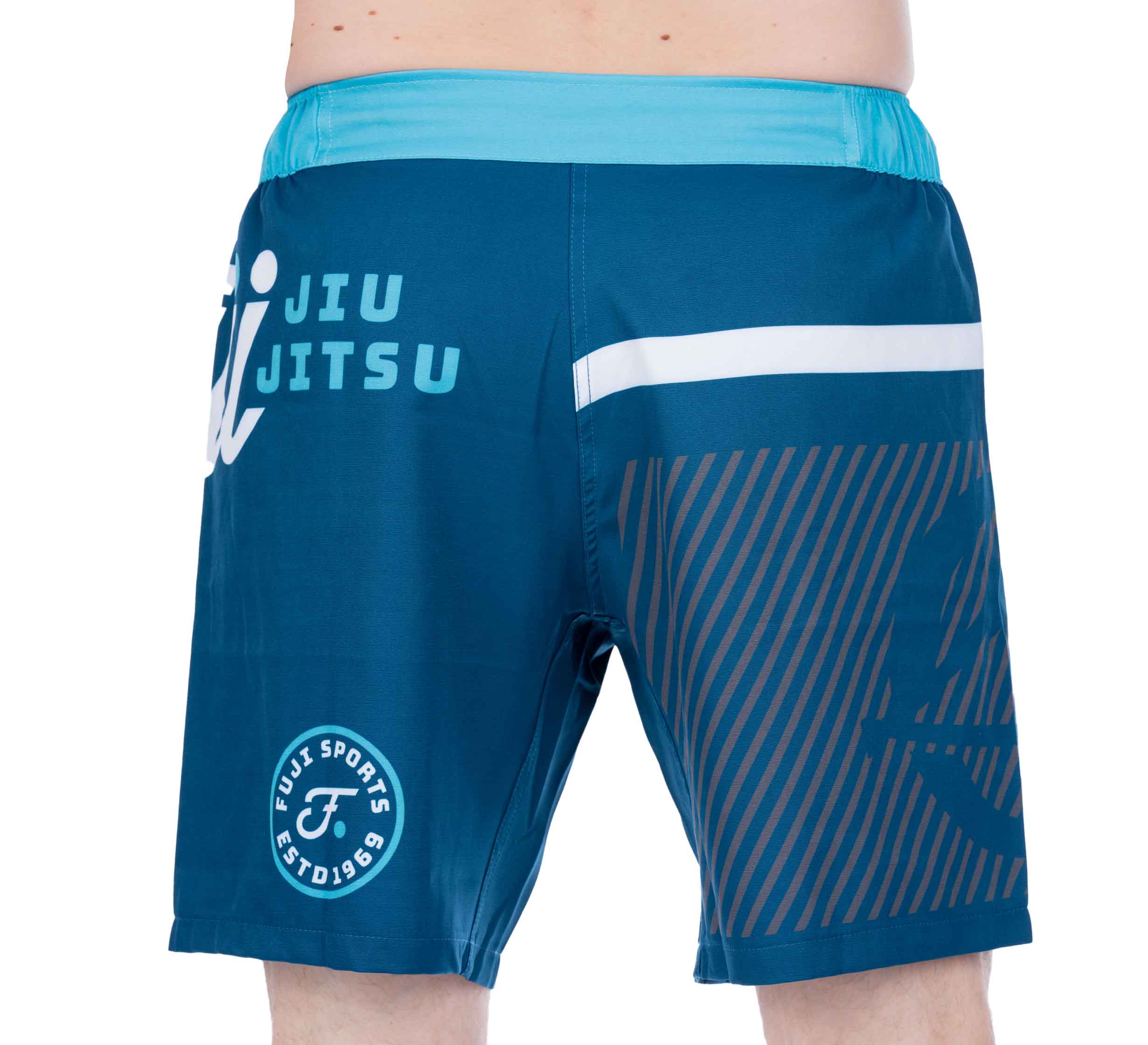 A person wearing Script Grappling Shorts Blue featuring "Jiu Jitsu" and "Fuji Sports" printed on the back left side, with white and brown diagonal stripe patterns.