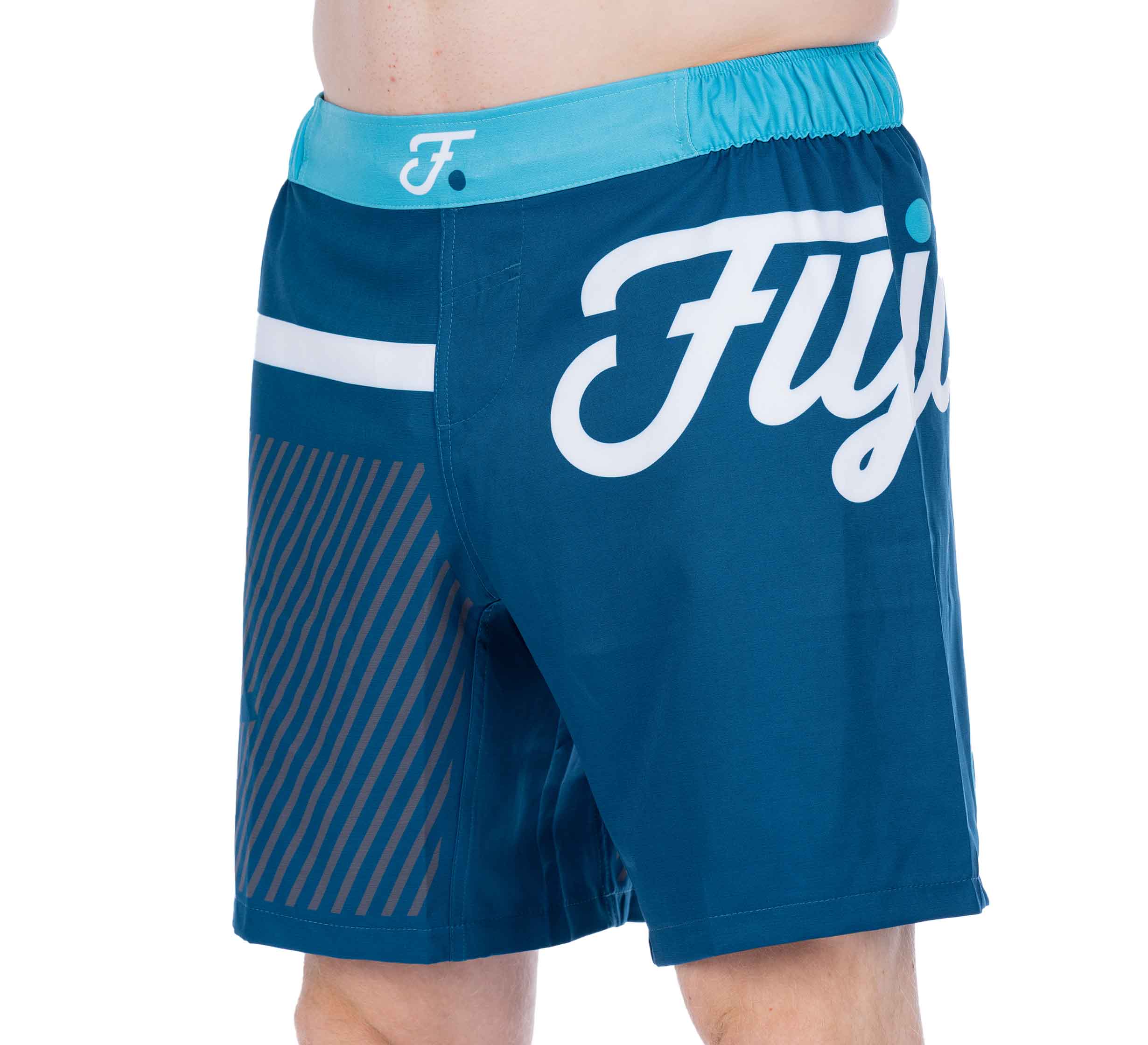 Someone wears Script Grappling Shorts Blue, featuring a teal waistband, white Fuji logo, a small white stripe, and diagonal brown lines on one side. Only the waist to mid-thigh area is shown.