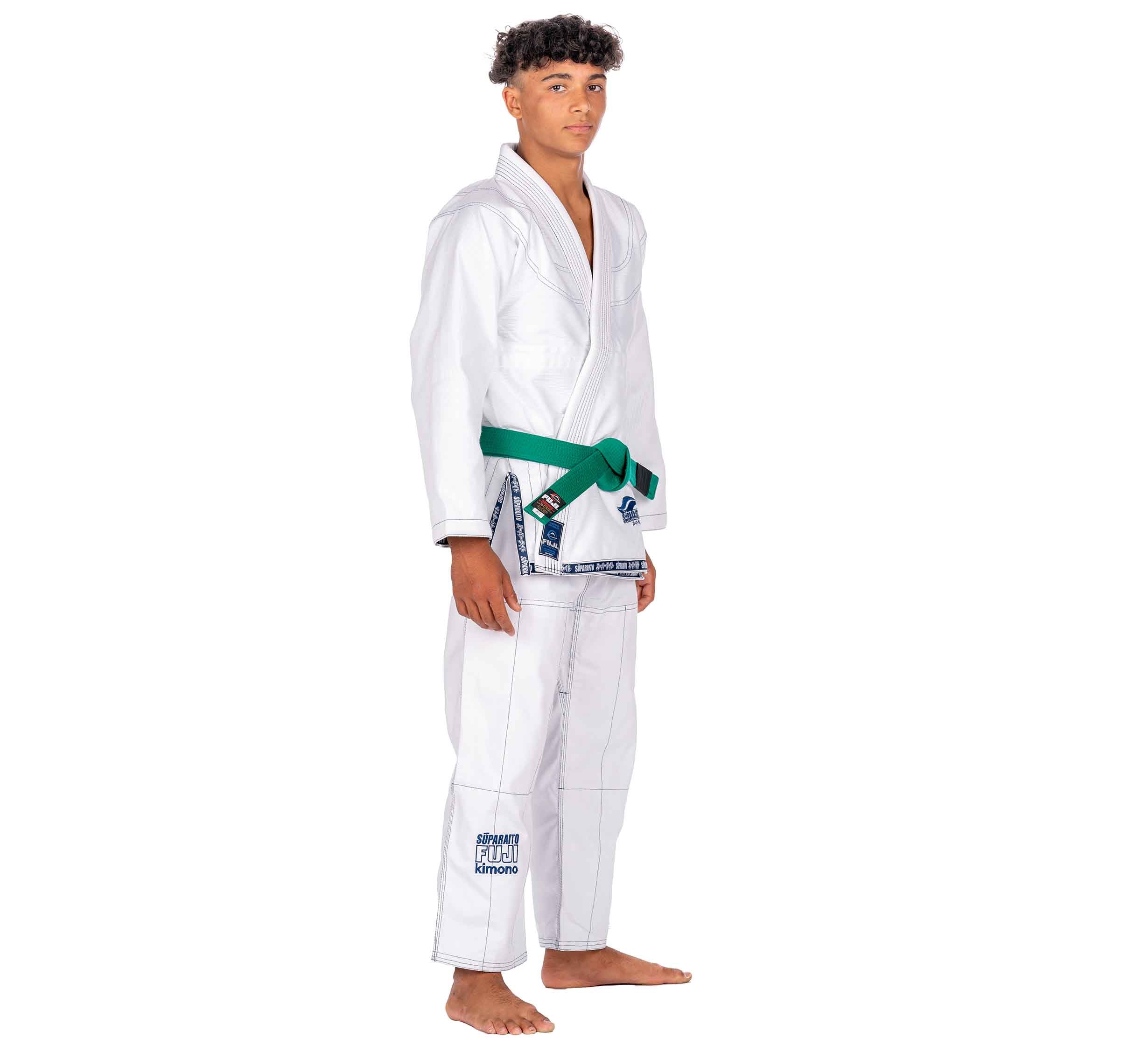 A young person stands barefoot in a Suparaito Kids White BJJ Gi with a green belt, facing slightly to the side against a plain white background.