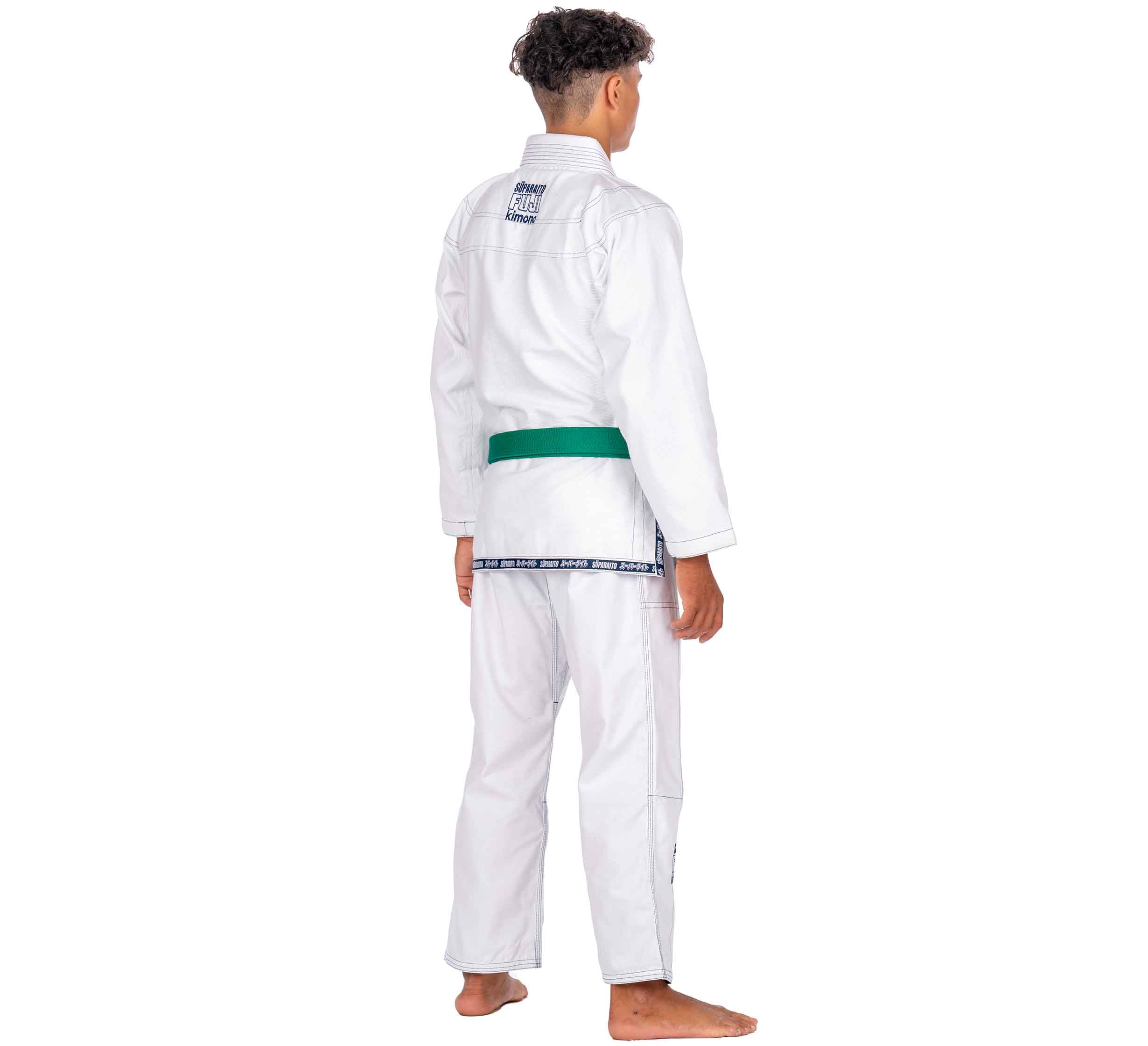 A child stands barefoot, back facing, wearing the Suparaito Kids White BJJ Gi with a green belt. A patch is visible on the upper back. The background is plain white.