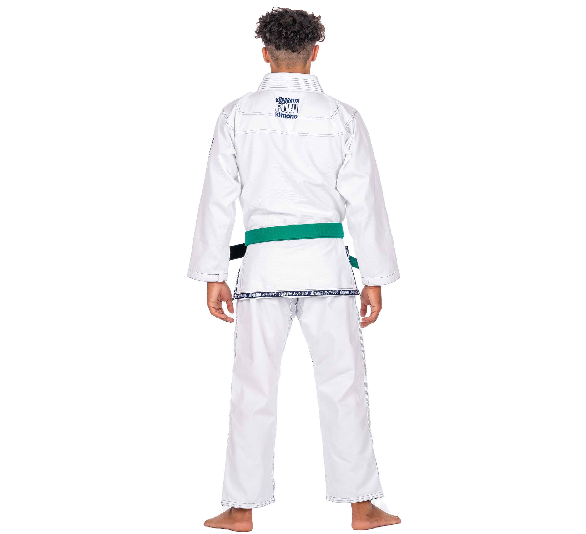 A barefoot child with curly hair, wearing the Suparaito Kids White BJJ Gi and a green belt, stands facing away from the camera against a plain white background.