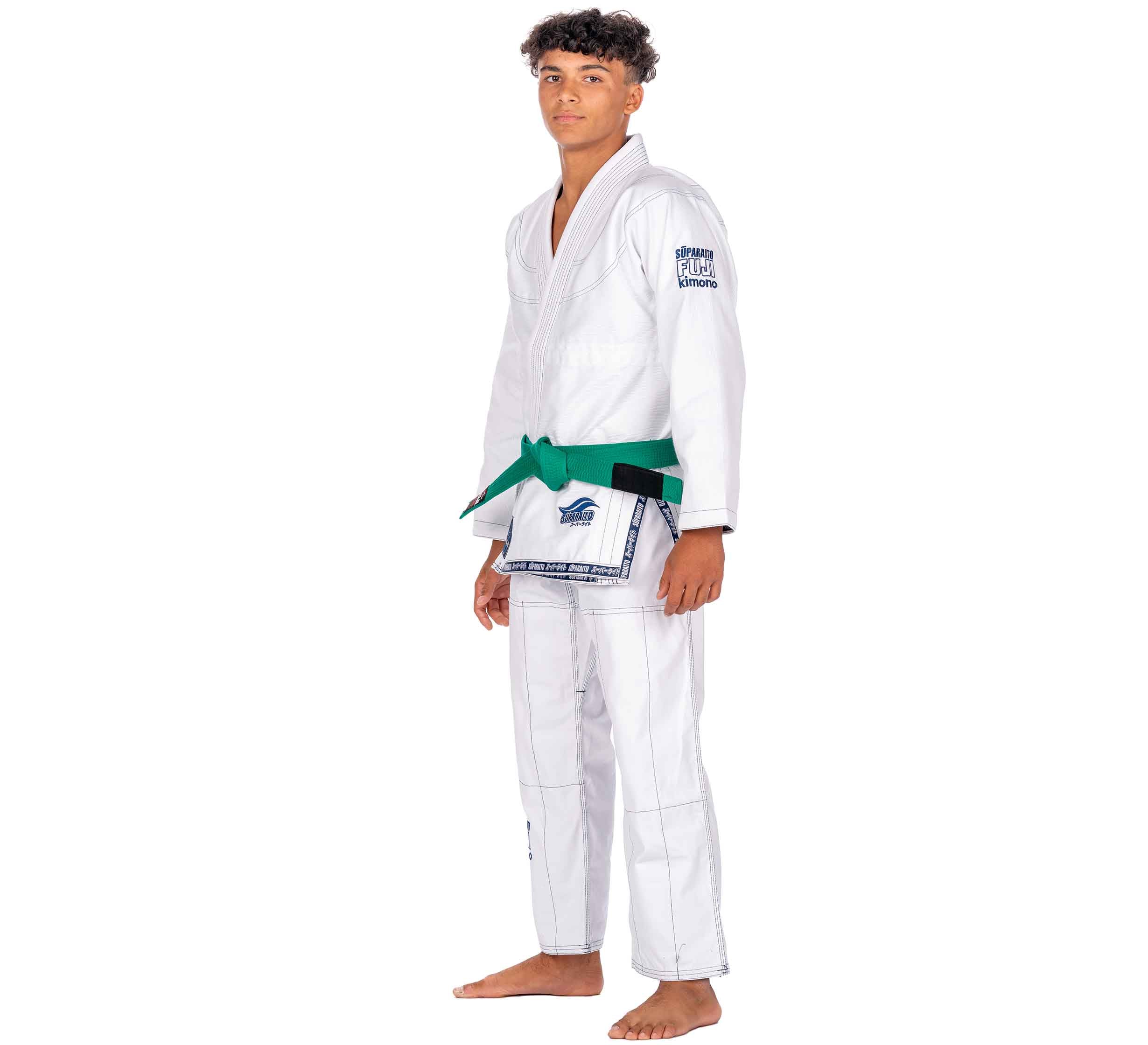 A young man stands barefoot, wearing the Suparaito Kids White BJJ Gi with a green belt, looking at the camera against a plain white background.