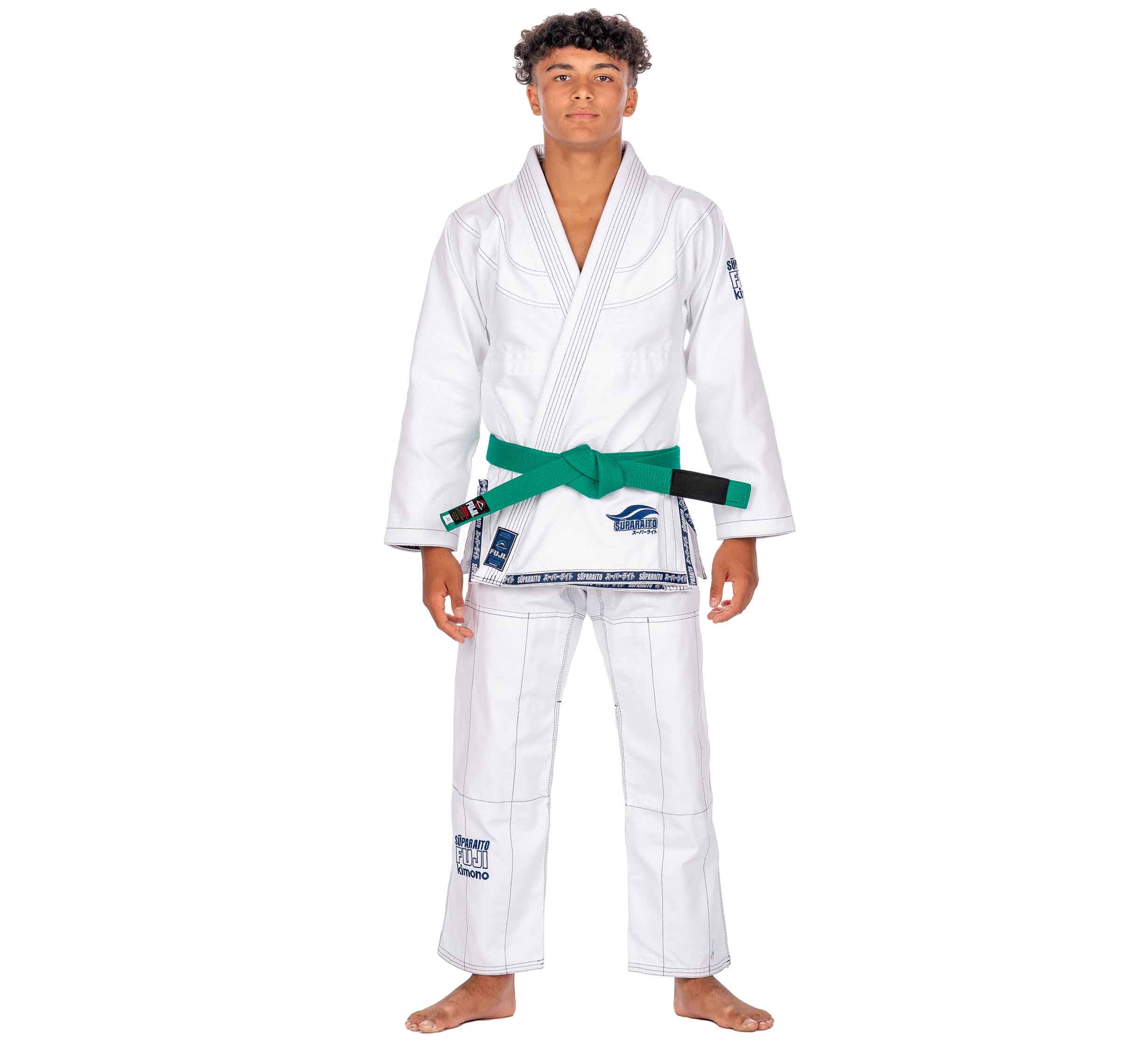 A young man with short curly hair stands barefoot, wearing the Suparaito Kids White BJJ Gi and a green belt, facing forward against a plain white background.