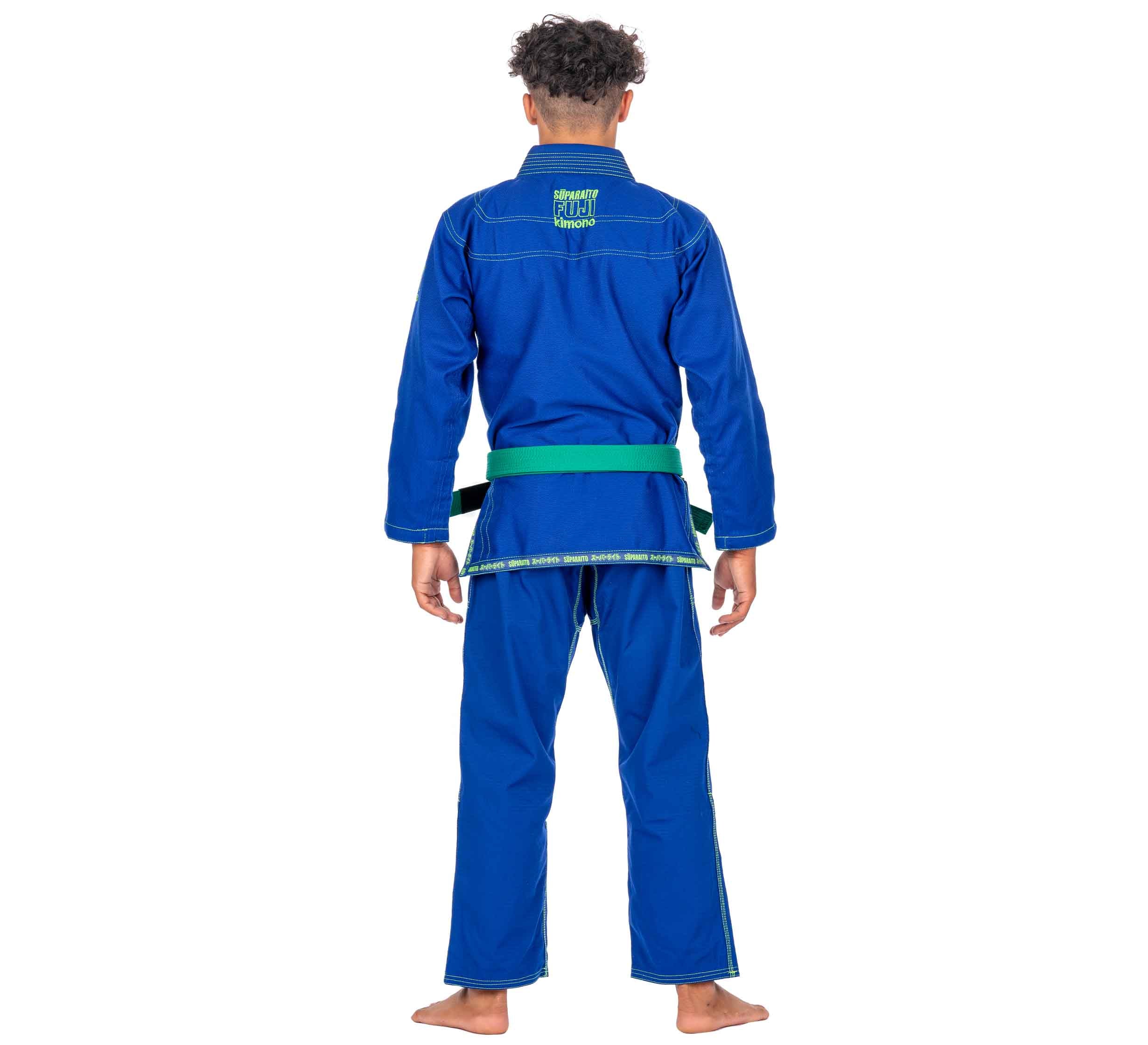 A person stands barefoot with their back to the camera, wearing the Suparaito Kids Blue BJJ Gi and a green belt.
