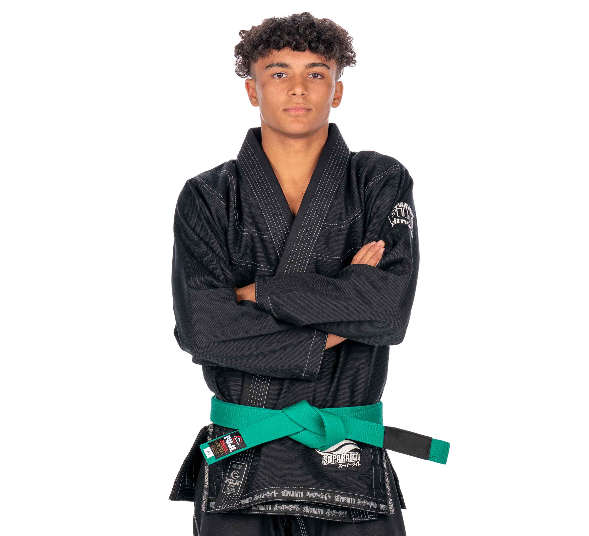 A confident young person with curly hair, arms crossed, wears the Suparaito Kids Black BJJ Gi and a green belt against a plain white background.