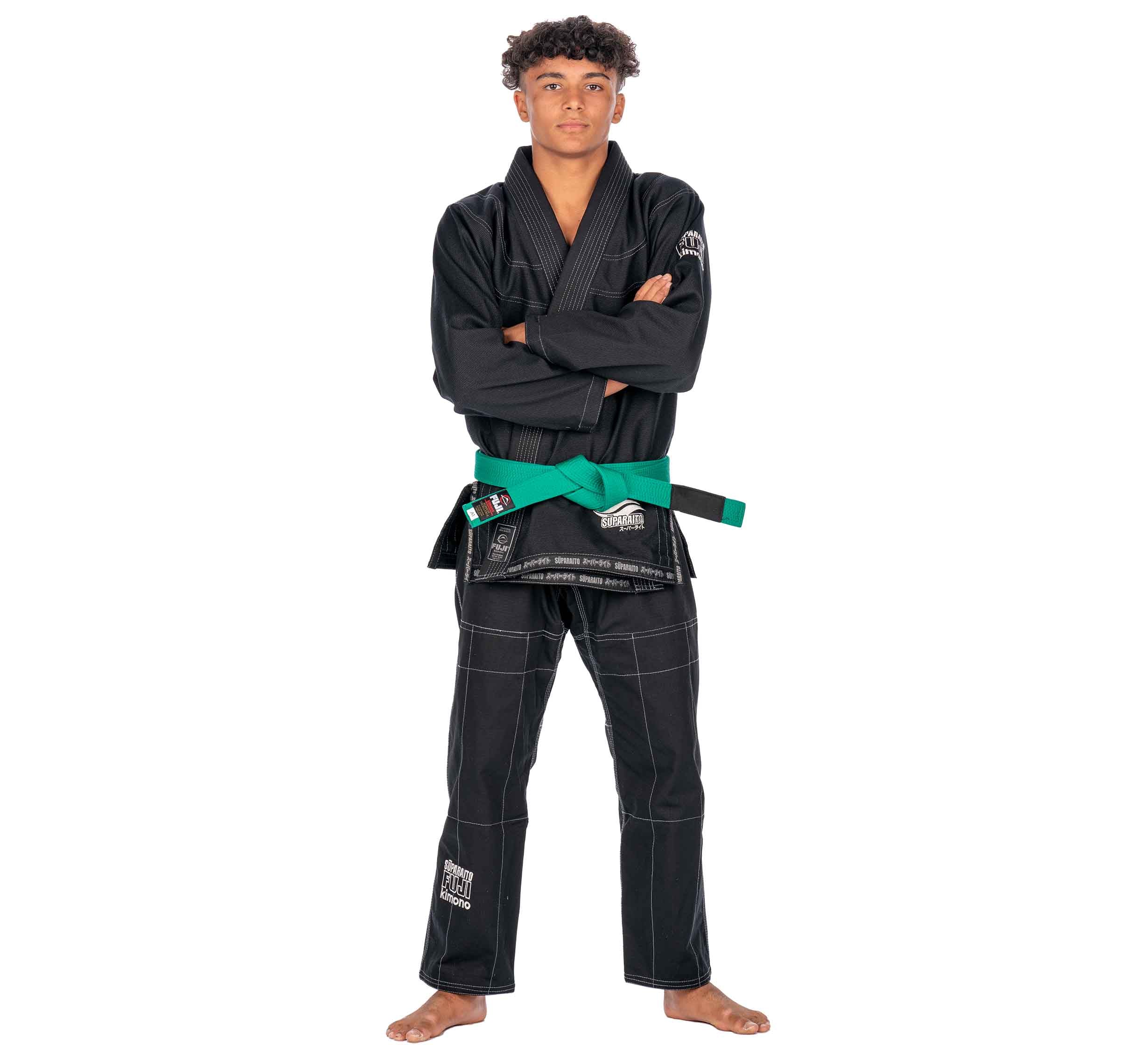 A young person stands barefoot, arms crossed, confidently modeling the Suparaito Kids Black BJJ Gi with a green belt against a plain white background.