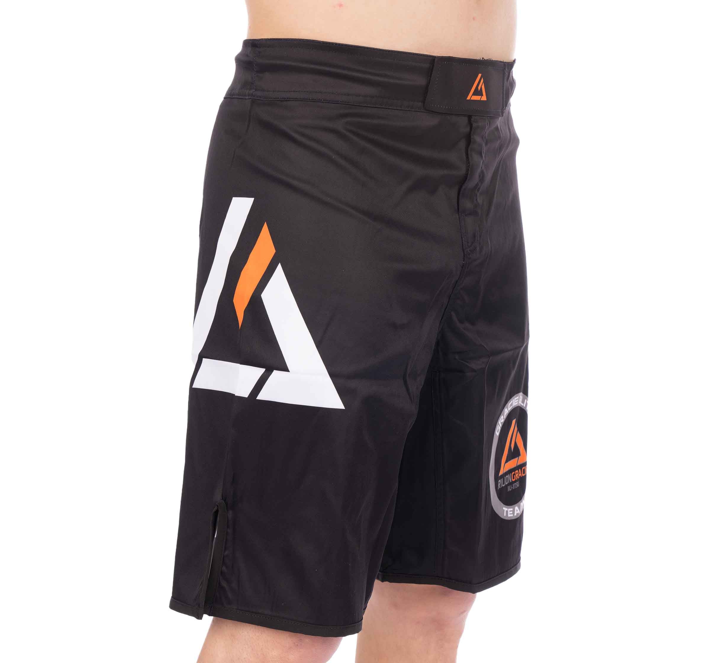 A person wearing Rilion Gracie Black Fight Shorts, featuring a white and orange geometric logo on the side and a matching circular patch on the lower leg.