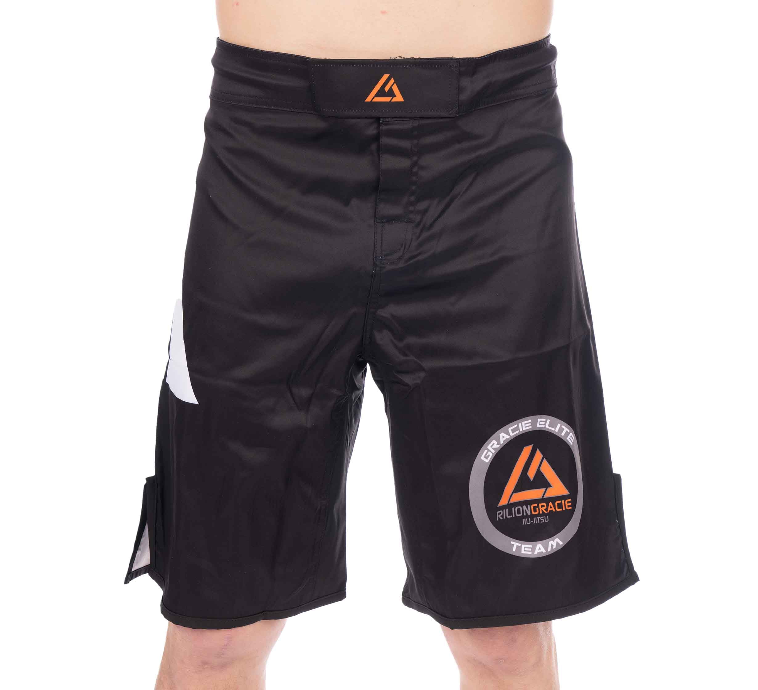 Someone wearing Rilion Gracie Black Fight Shorts featuring orange and white logos and text, including Gracie Elite and Rilion Gracie Team, stands against a white background.