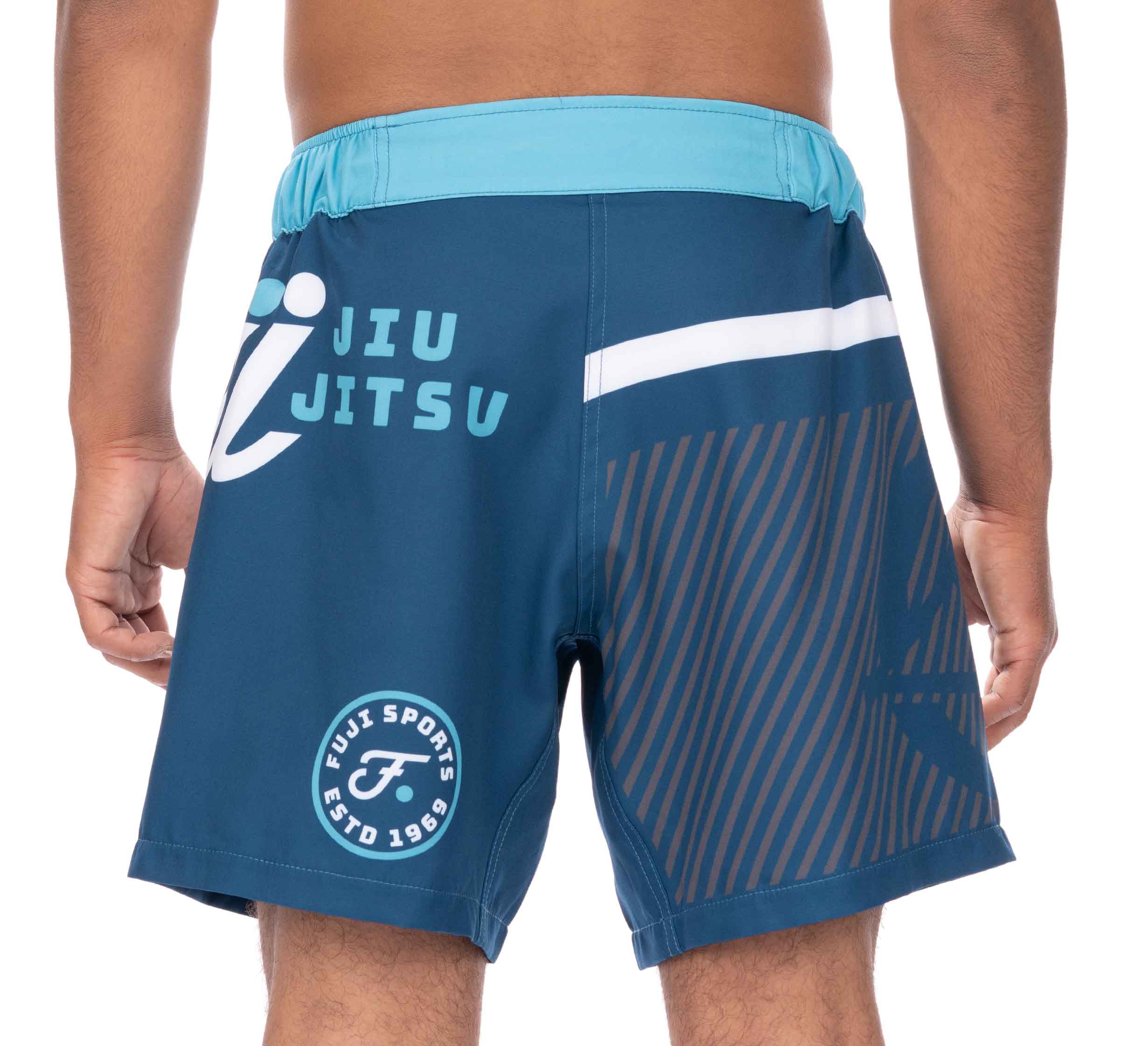 A person is wearing Script Grappling Shorts Blue with "JIU JITSU" and "FUJI SPORTS ESTD 1969" printed on the back, graphic designs, and a light blue waistband.