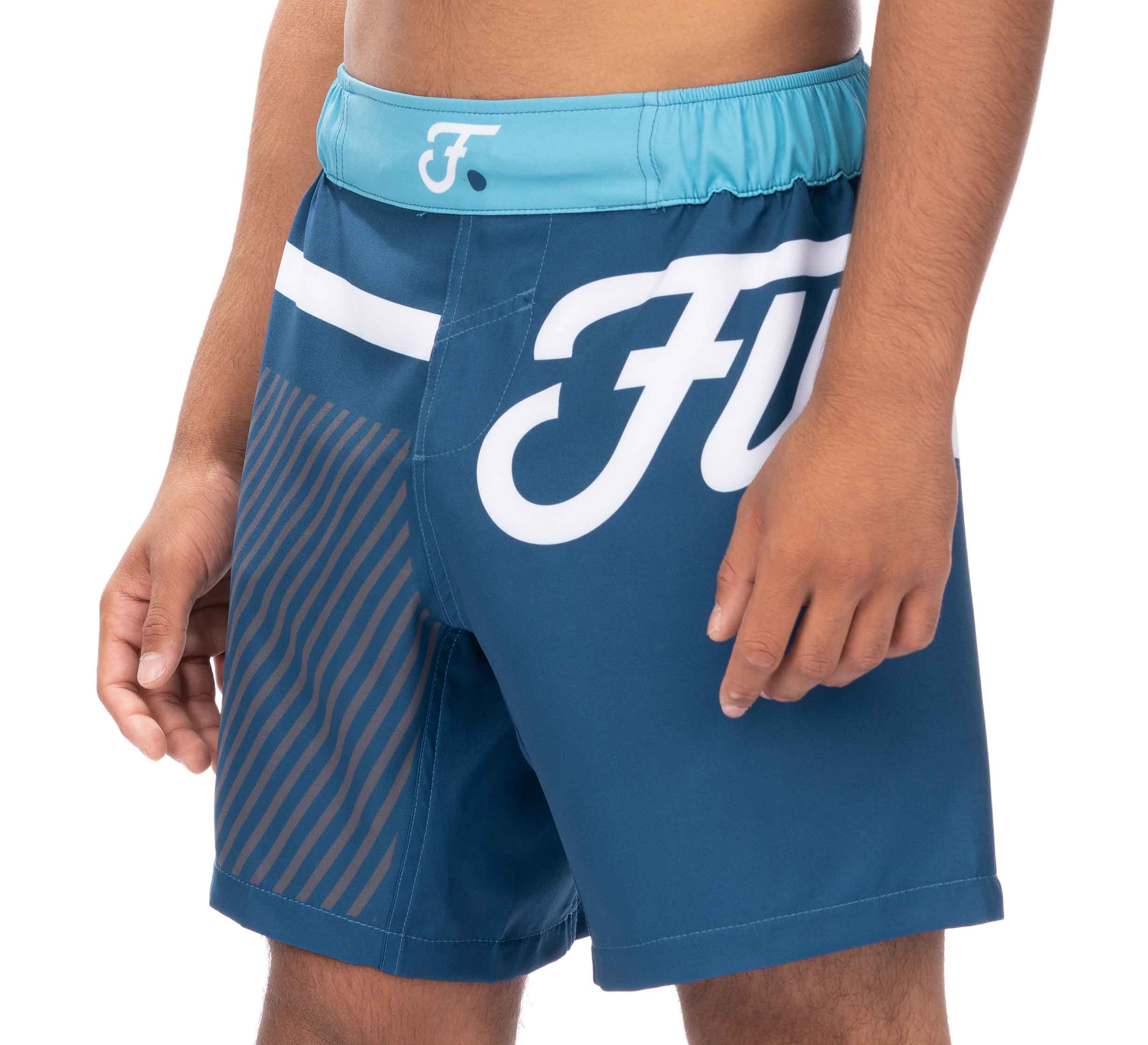 A person wearing Script Grappling Shorts Blue, featuring a turquoise waistband, large white stylized F logo on the side, and diagonal stripes on one leg.