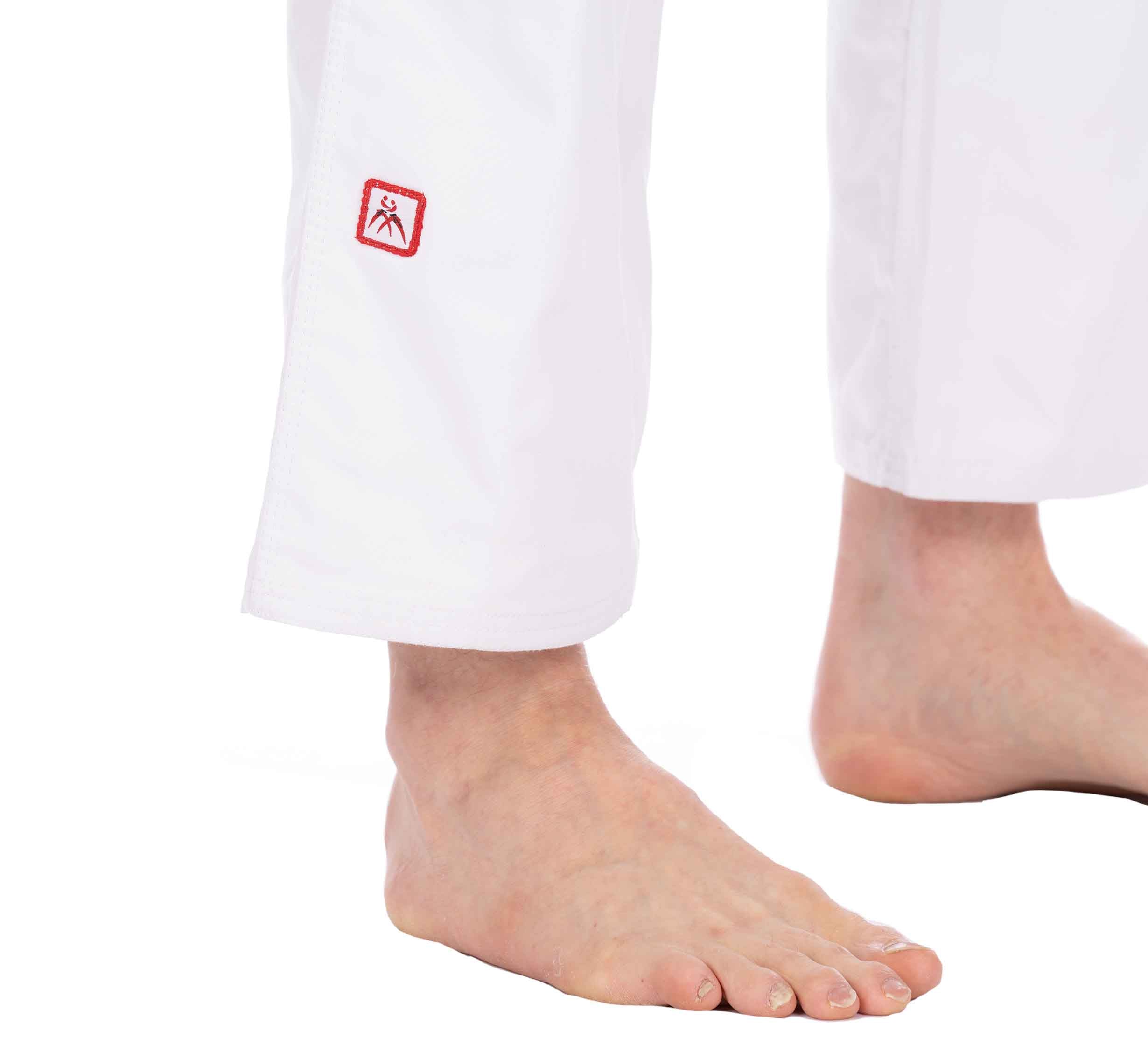 Close-up of bare feet and lower legs in USA Judo Single Weave Gi 2.0 White pants, featuring a small red and white patch near the hem against a plain white background.