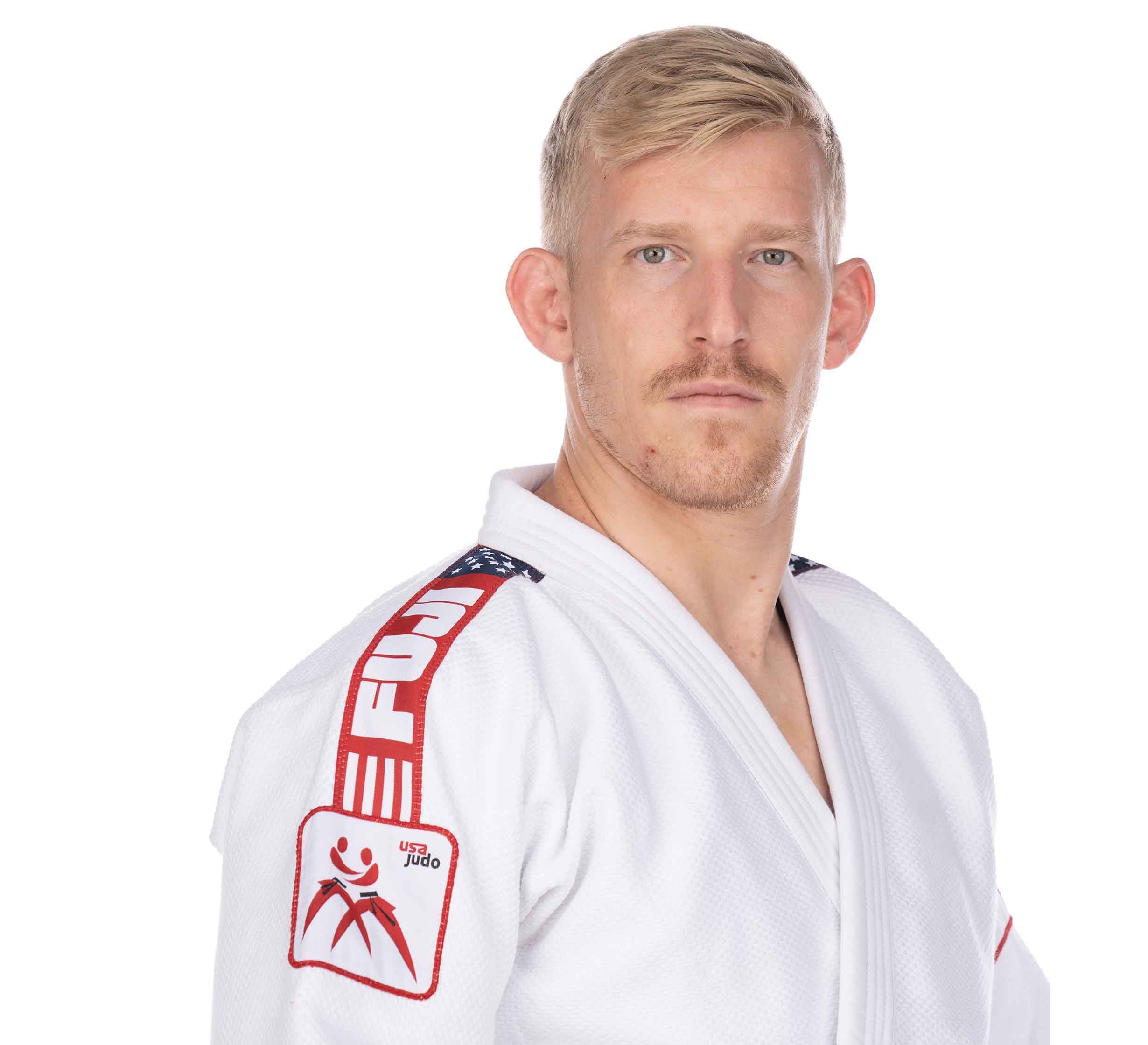 A man with short blond hair and a mustache wears the USA Judo Single Weave Gi 2.0 White, featuring red FUJI branding and a USA Judo patch, standing against a plain white background.