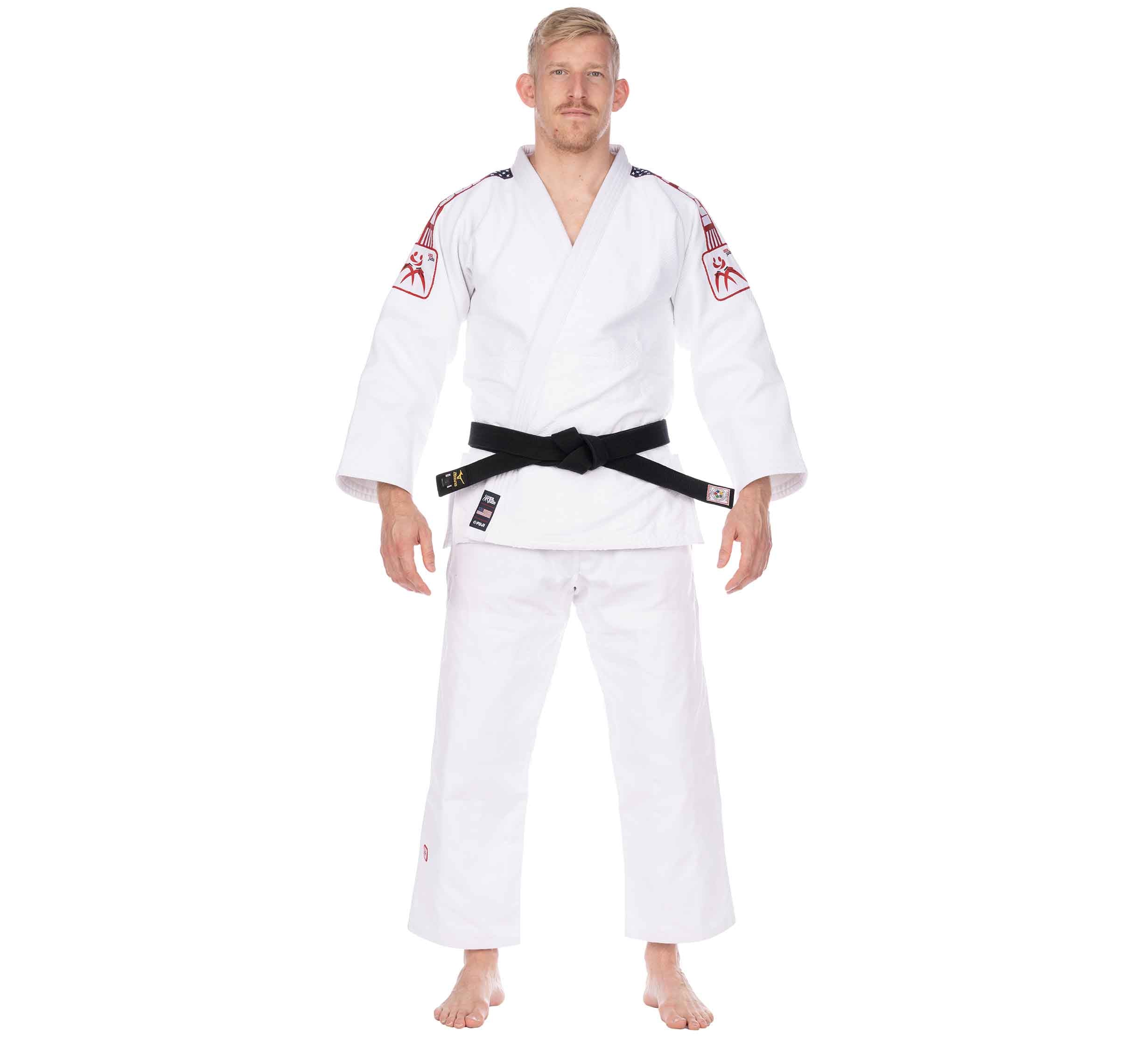 A man stands barefoot, facing forward with a neutral expression, wearing the USA Judo Single Weave Gi 2.0 White and a black belt. The gi features red patches on the shoulders and sleeves, set against a white background.