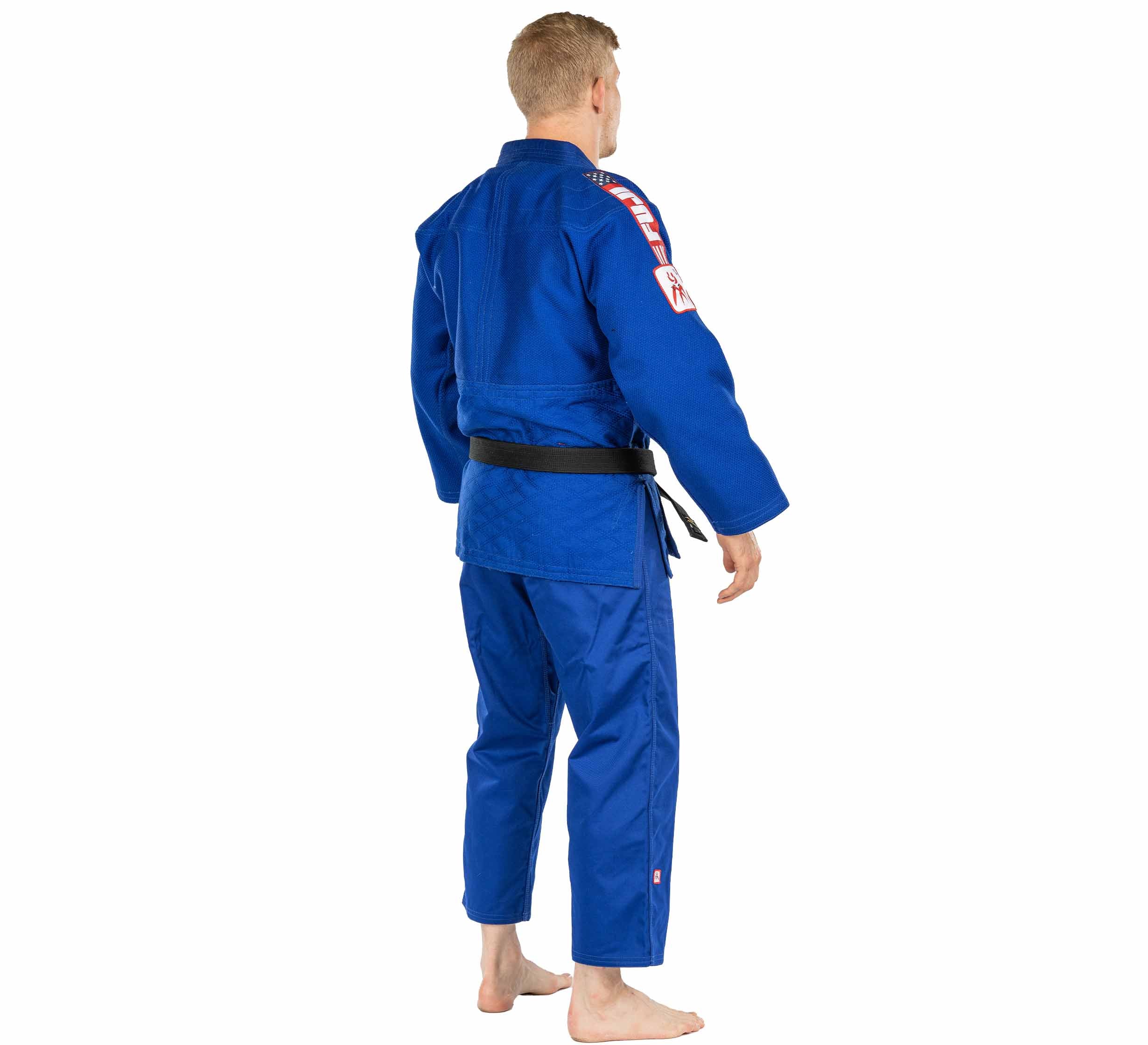 A person stands barefoot facing away, showing embroidered patches on the shoulder and arm of the USA Judo Single Weave Gi 2.0 Blue with black belt.