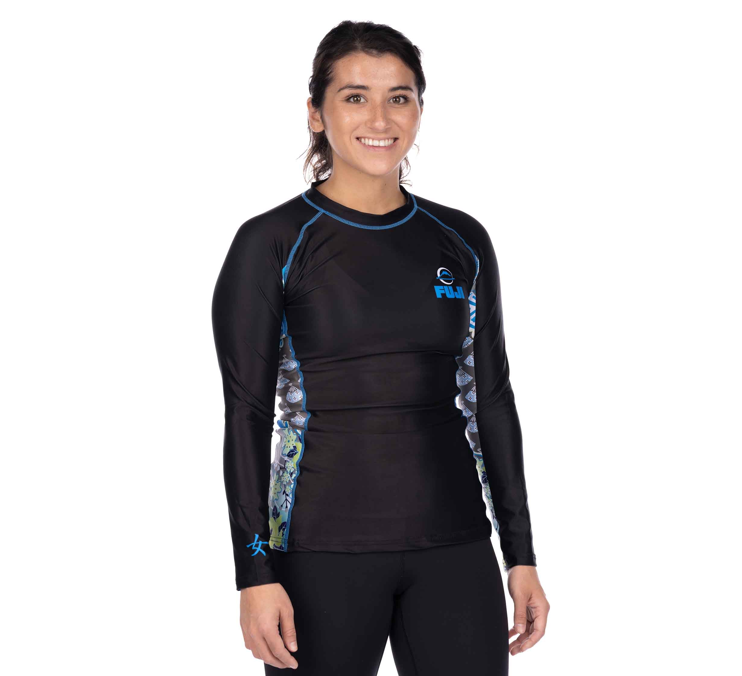 A woman with dark hair tied back is smiling and wearing the Kimono Kid's Long Sleeve Rashguard Blue, standing against a plain white background.