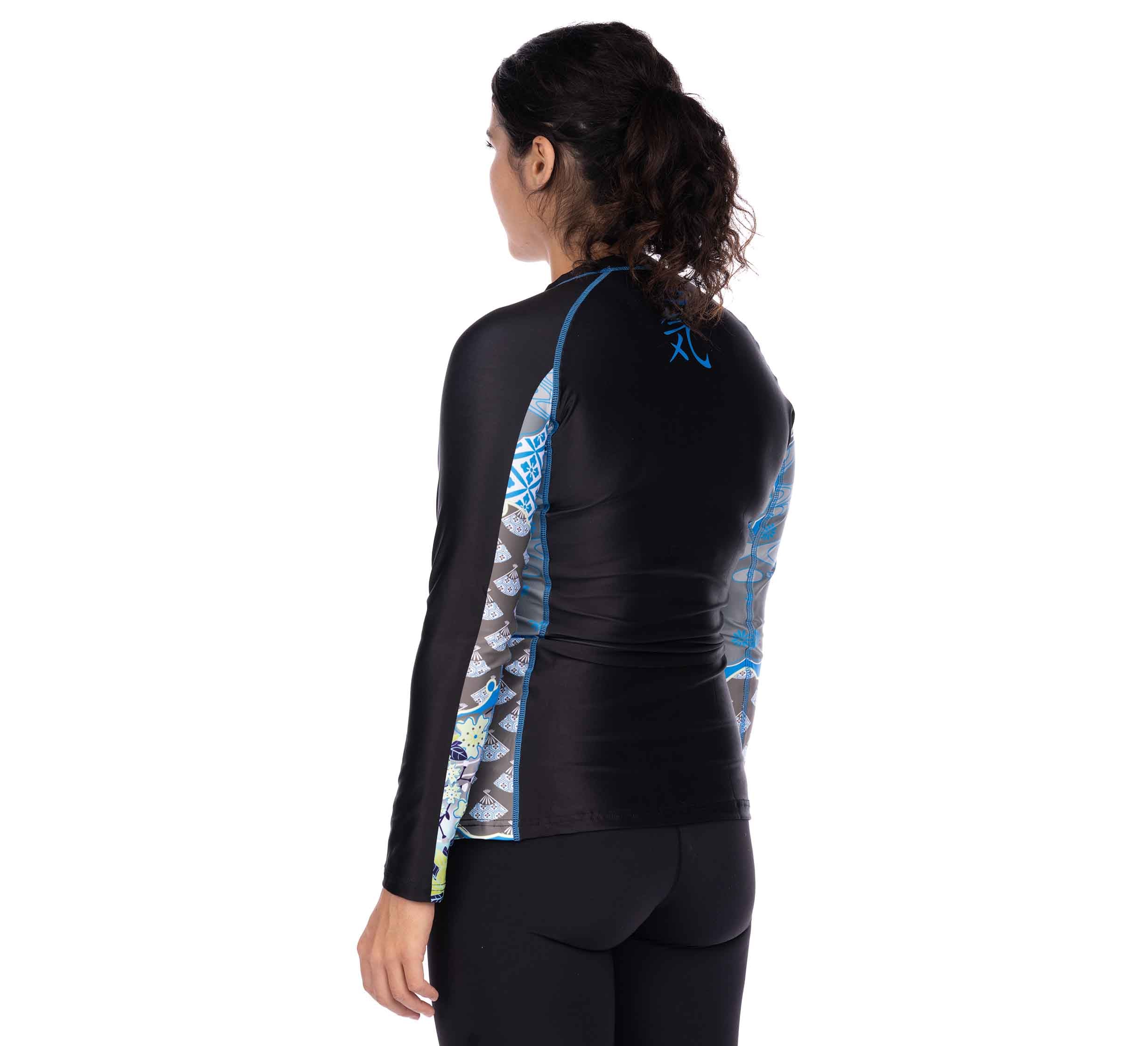A woman with dark, curly hair tied back is seen from behind wearing the Kimono Kid's Long Sleeve Rashguard Blue and black leggings against a plain white background.