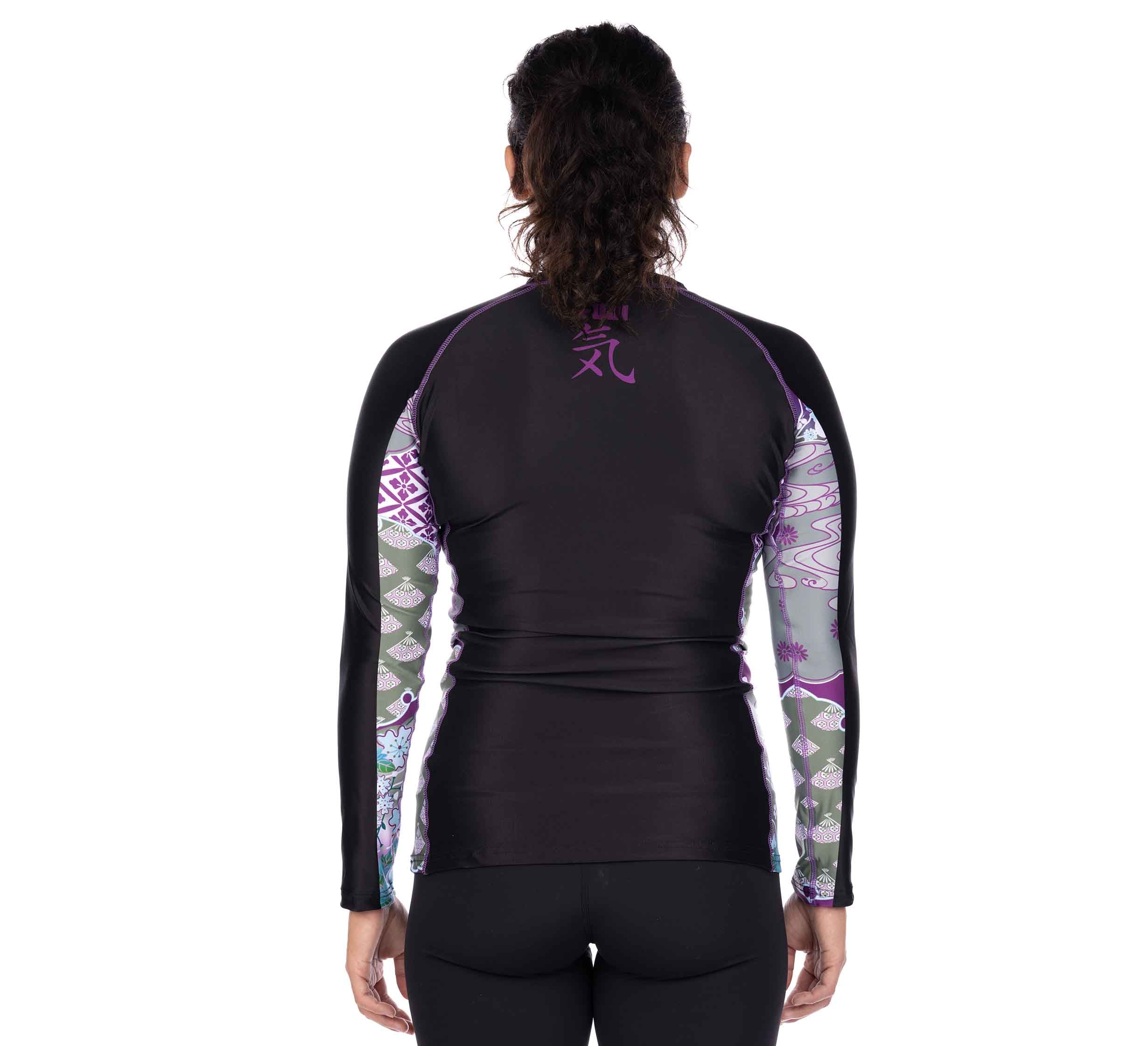 A person with curly hair in a ponytail faces away, wearing the Kimono Womens Long Sleeve Rashguard Purple with black and purple patterned sleeves, paired with black leggings.
