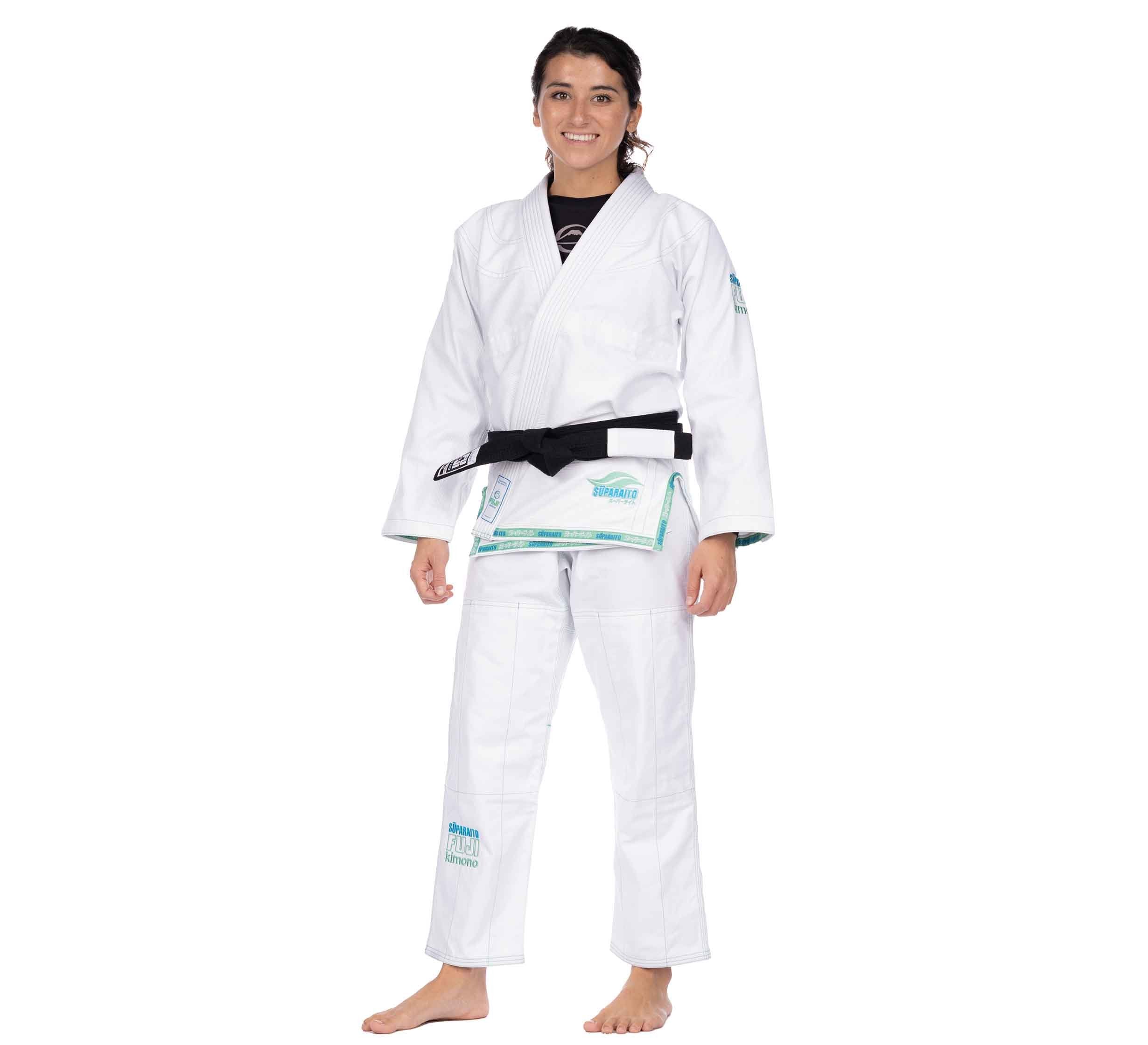 A woman wearing the Suparaito Girl's BJJ Gi in teal, barefoot and smiling, stands against a plain white background.
