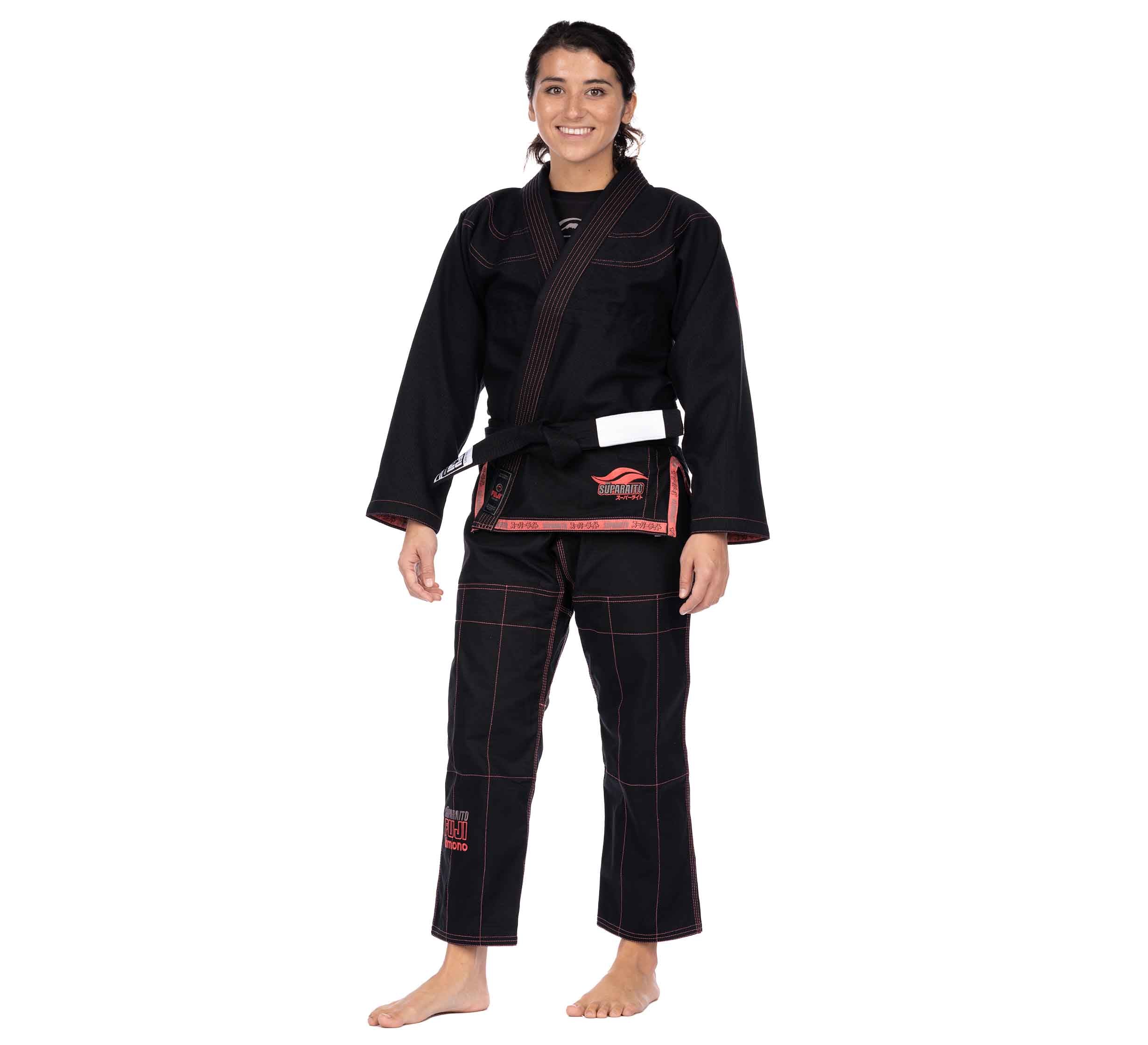 A person stands barefoot, smiling, and wearing the Suparaito Womens BJJ Gi in pink with a belt tied at the waist against a plain white background.