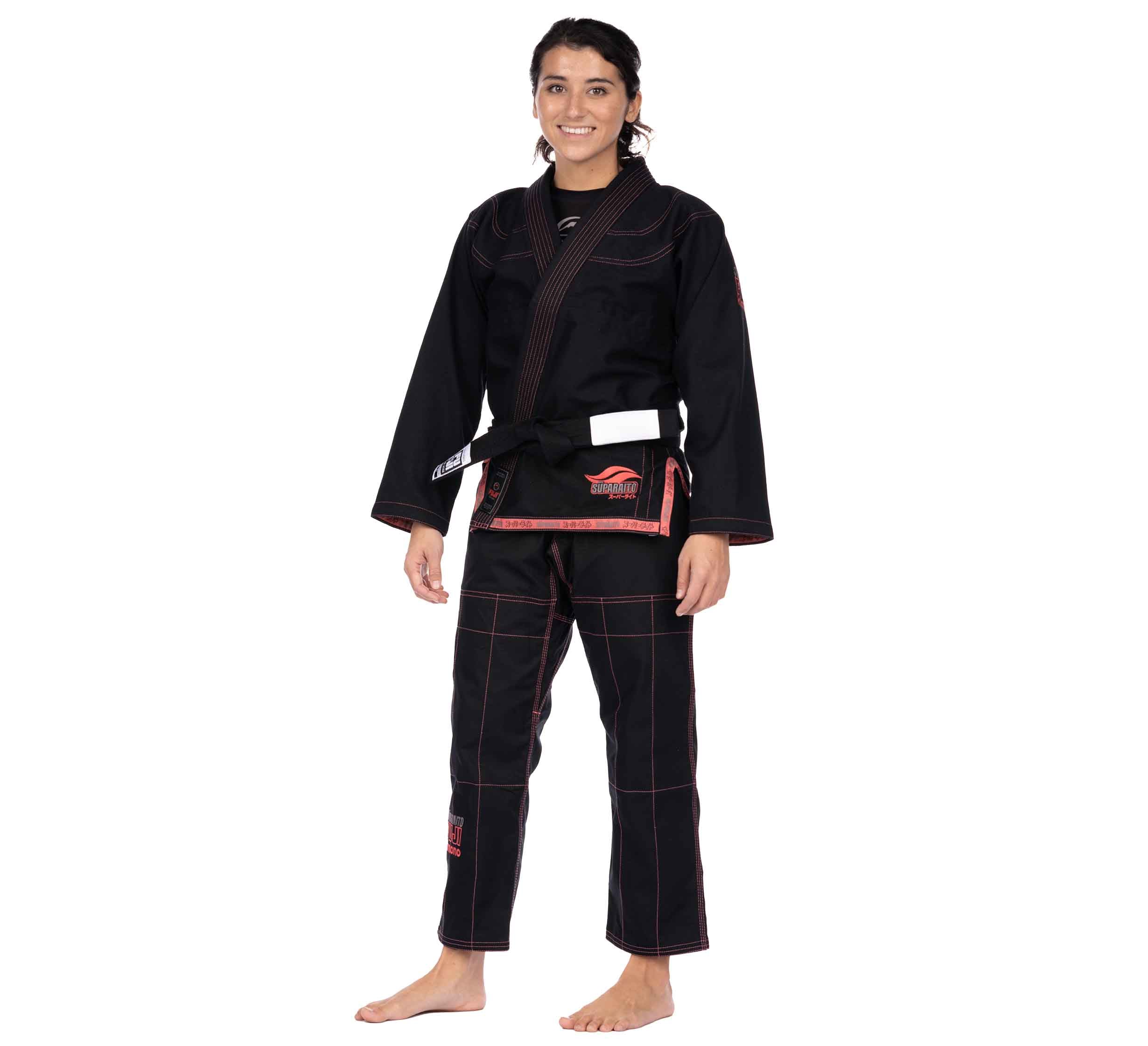 A smiling woman stands barefoot, wearing the Suparaito Womens BJJ Gi in pink with a black belt, facing forward against a plain white background.
