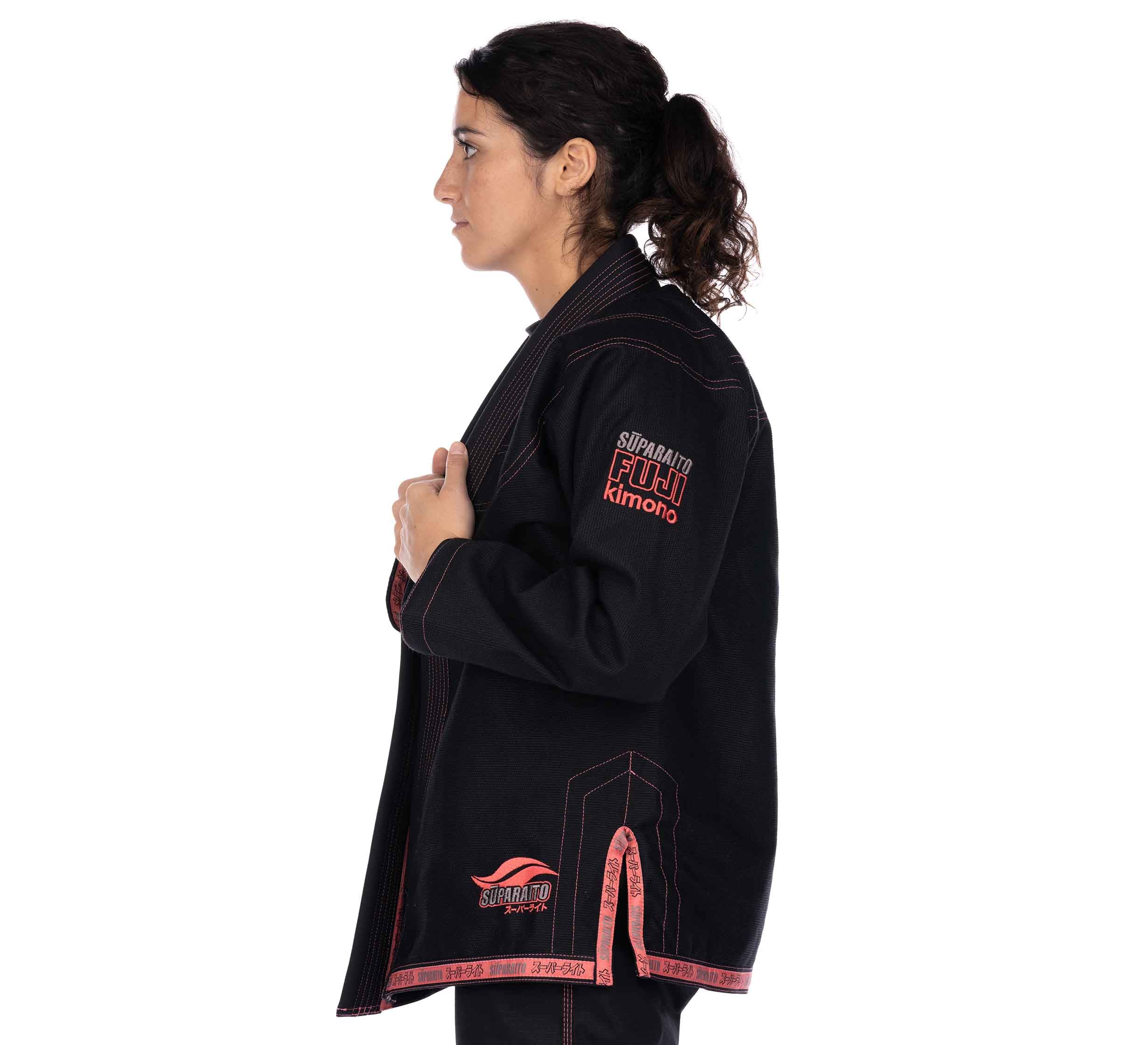 A woman with curly hair in a ponytail stands in profile against a plain white background, wearing the Suparaito Women's BJJ Gi in pink.
