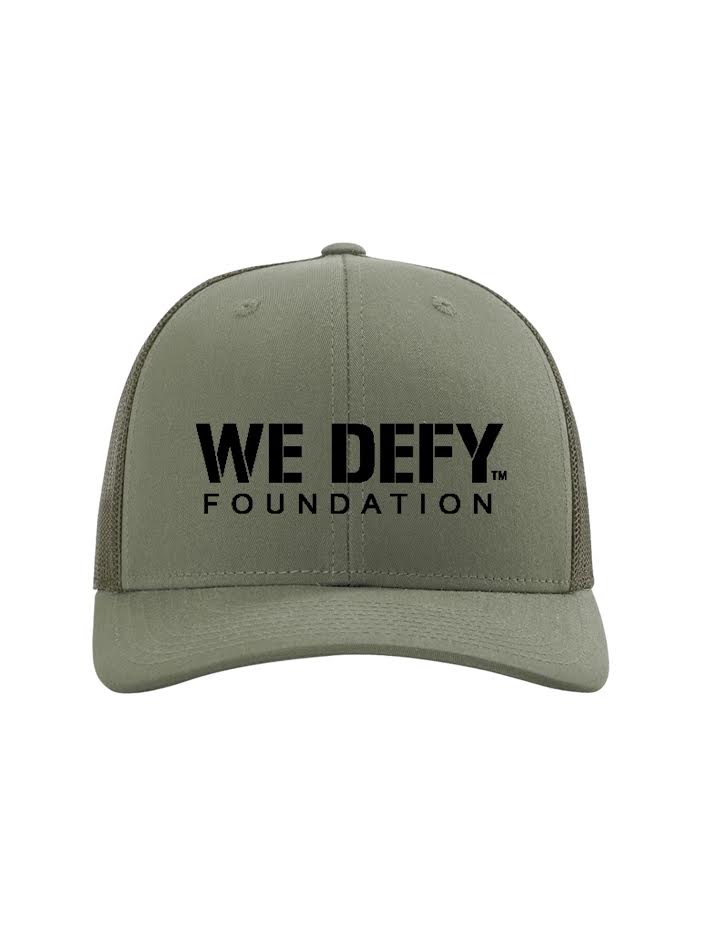 A green We Defy Trucker Hat featuring the WE DEFY FOUNDATION printed in bold black letters on the front panel.