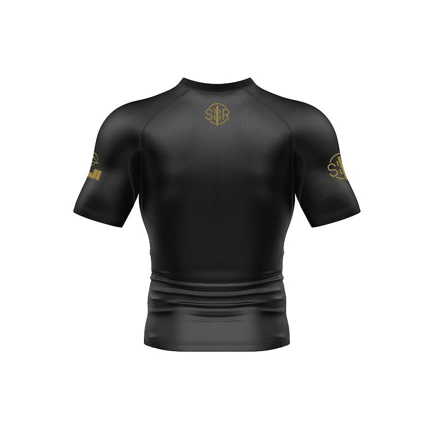 The Sheepdog Response Essential Short Sleeve Rashguard in black is shown from the back with subtle gold logos on the upper back and both sleeves, set against a white background.
