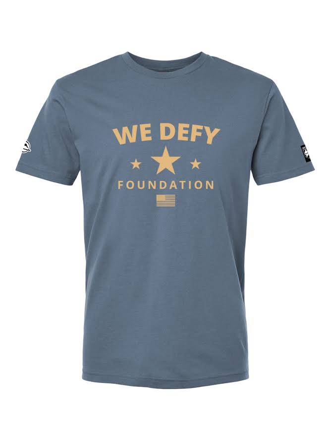 We Defy Retro Star Blue t-shirt featuring “WE DEFY FOUNDATION” and three tan stars printed on the chest, along with a small American flag below the text.