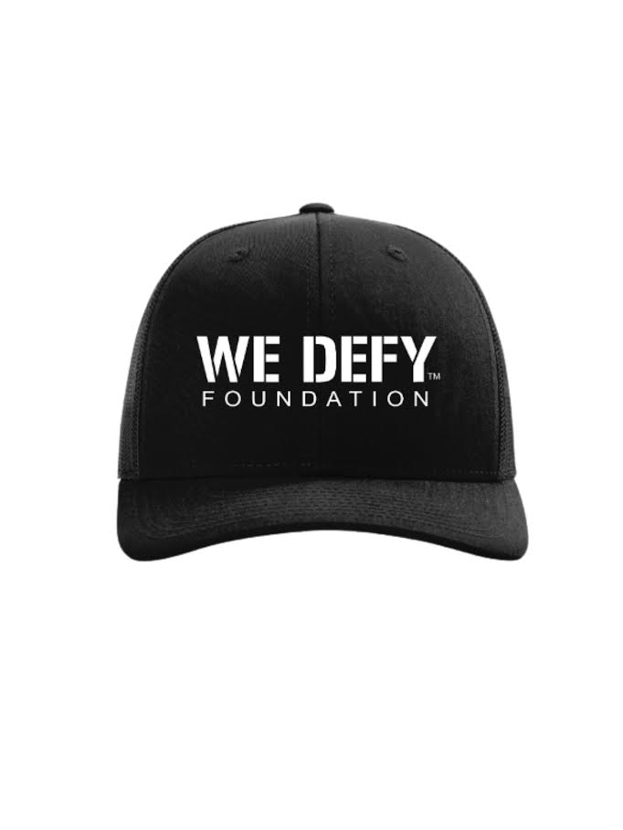 The We Defy Trucker Hat Black features bold white "WE DEFY FOUNDATION" lettering on the front.
