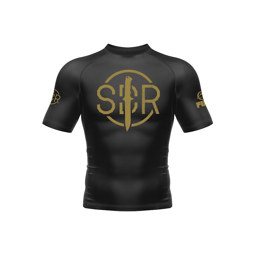 The Sheepdog Response Essential Short Sleeve Rashguard in black features gold SBR lettering and logos, a vertical sword design on the front, and additional logos on both sleeves.