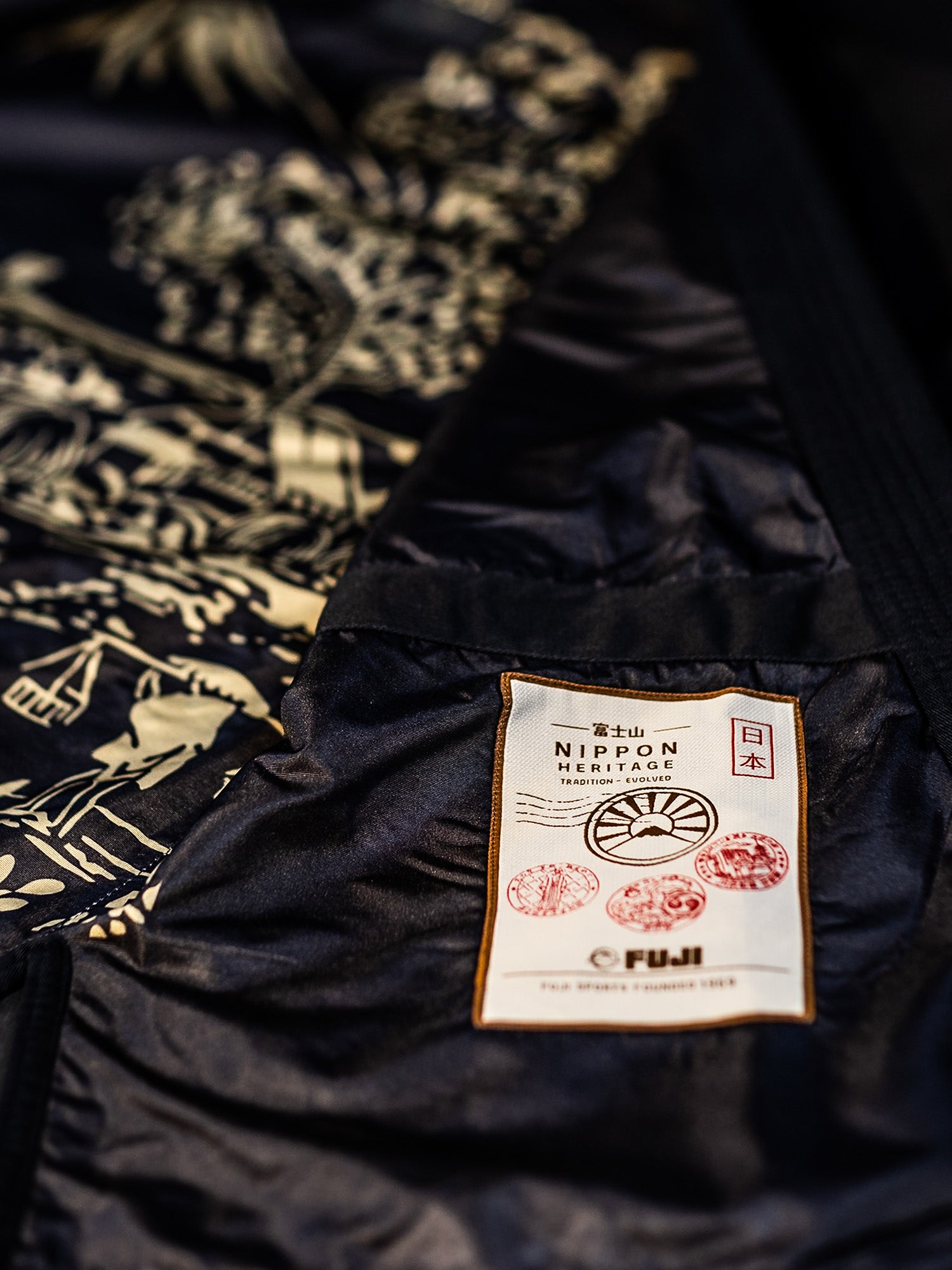 A close-up of the Heritage Keisho Lightweight BJJ Gi Black reveals a white label adorned with red stamps and Japanese text, while its lining showcases an intricate, traditional-style illustration.