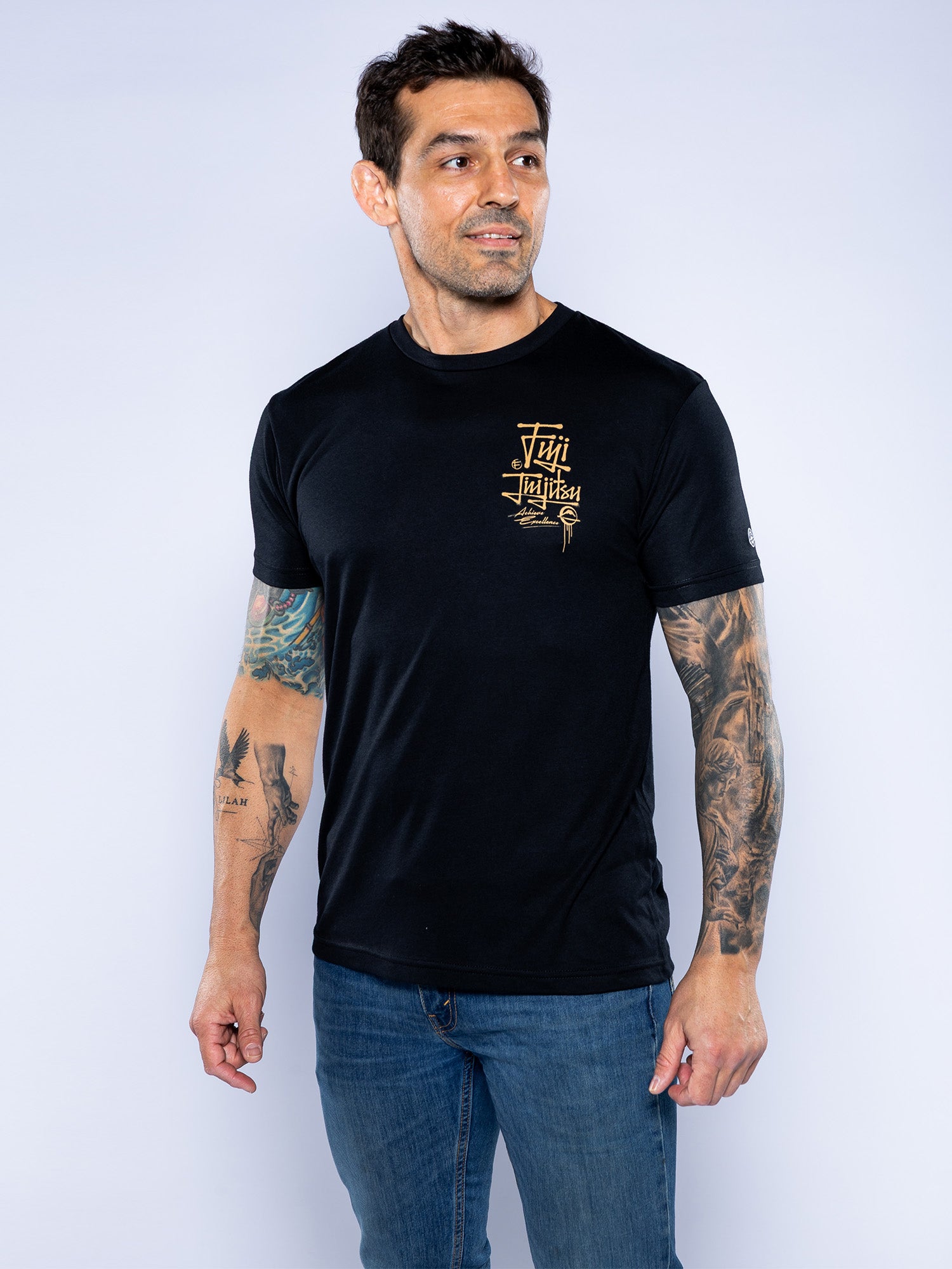 A man with tattoos wears the Japanese Street Art Shirt Black, featuring gold text and design on the chest, as he stands against a light background looking to his left.