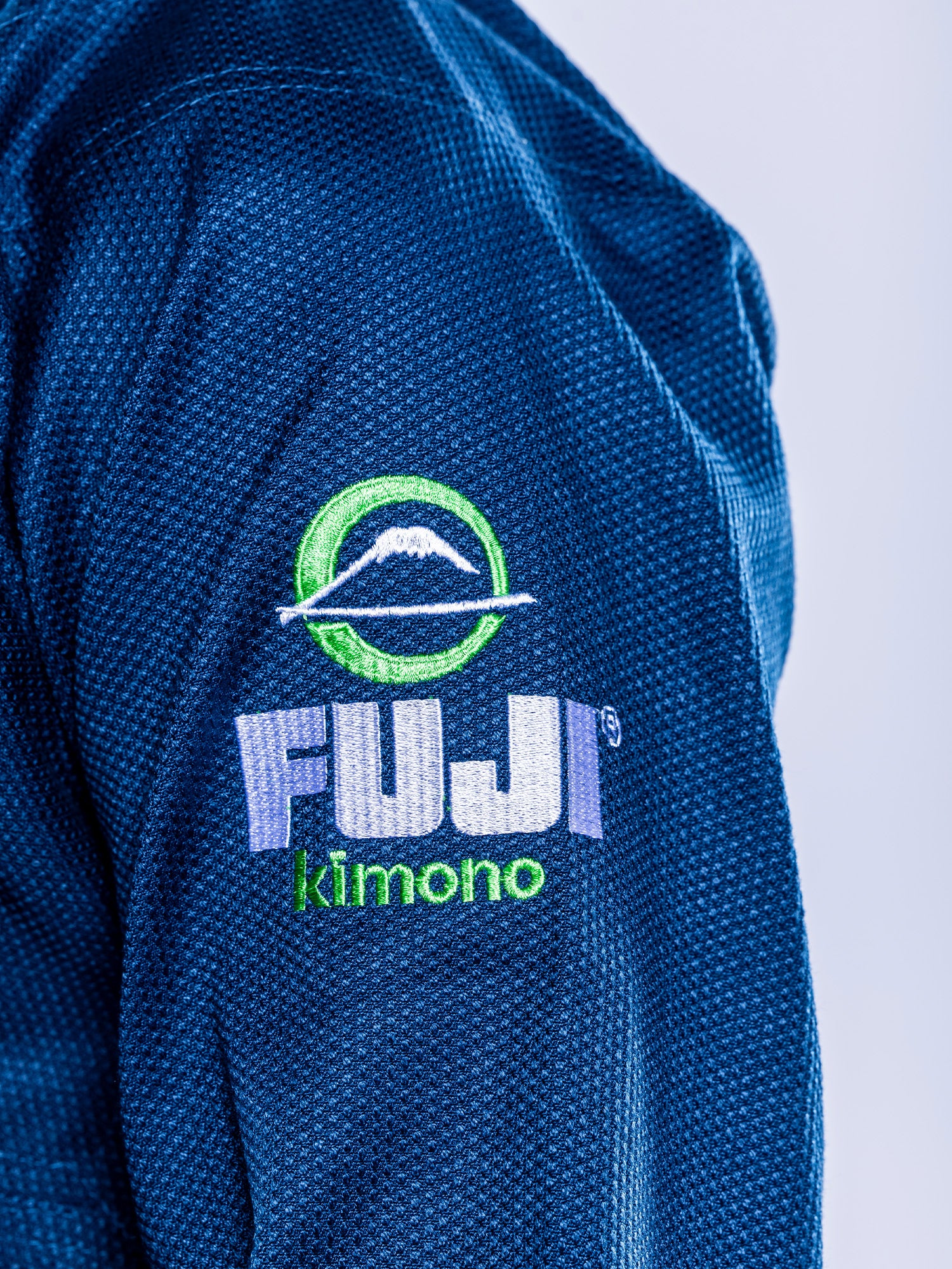 Close-up of the embroidered FUJI logo and mountain graphic on the sleeve of the Lightweight BJJ Gi Navy, a blue textured martial arts uniform.