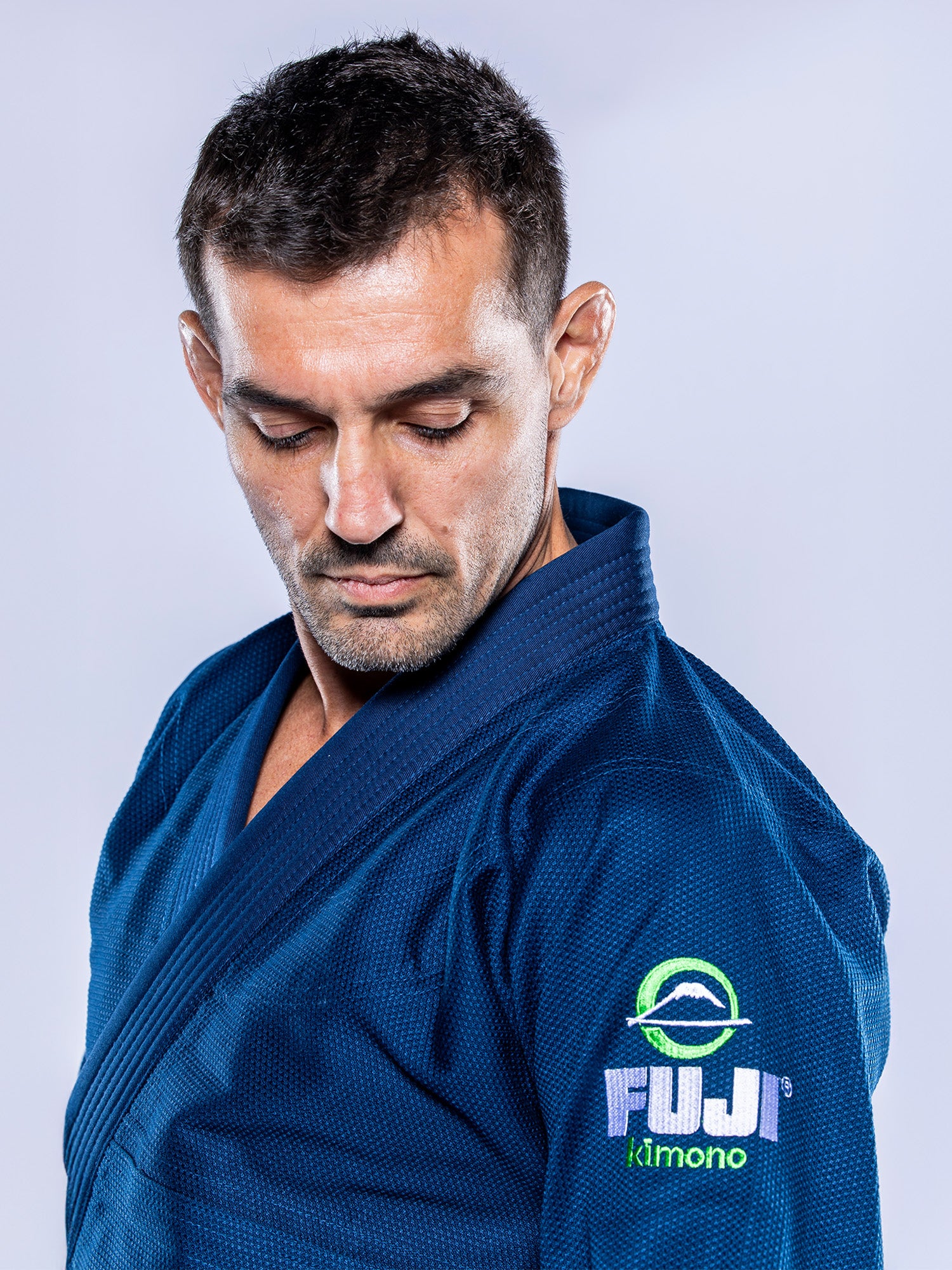 A man wears the Lightweight BJJ Gi Navy, featuring a Fuji Kimono logo on the sleeve, and looks down against a plain light gray background.