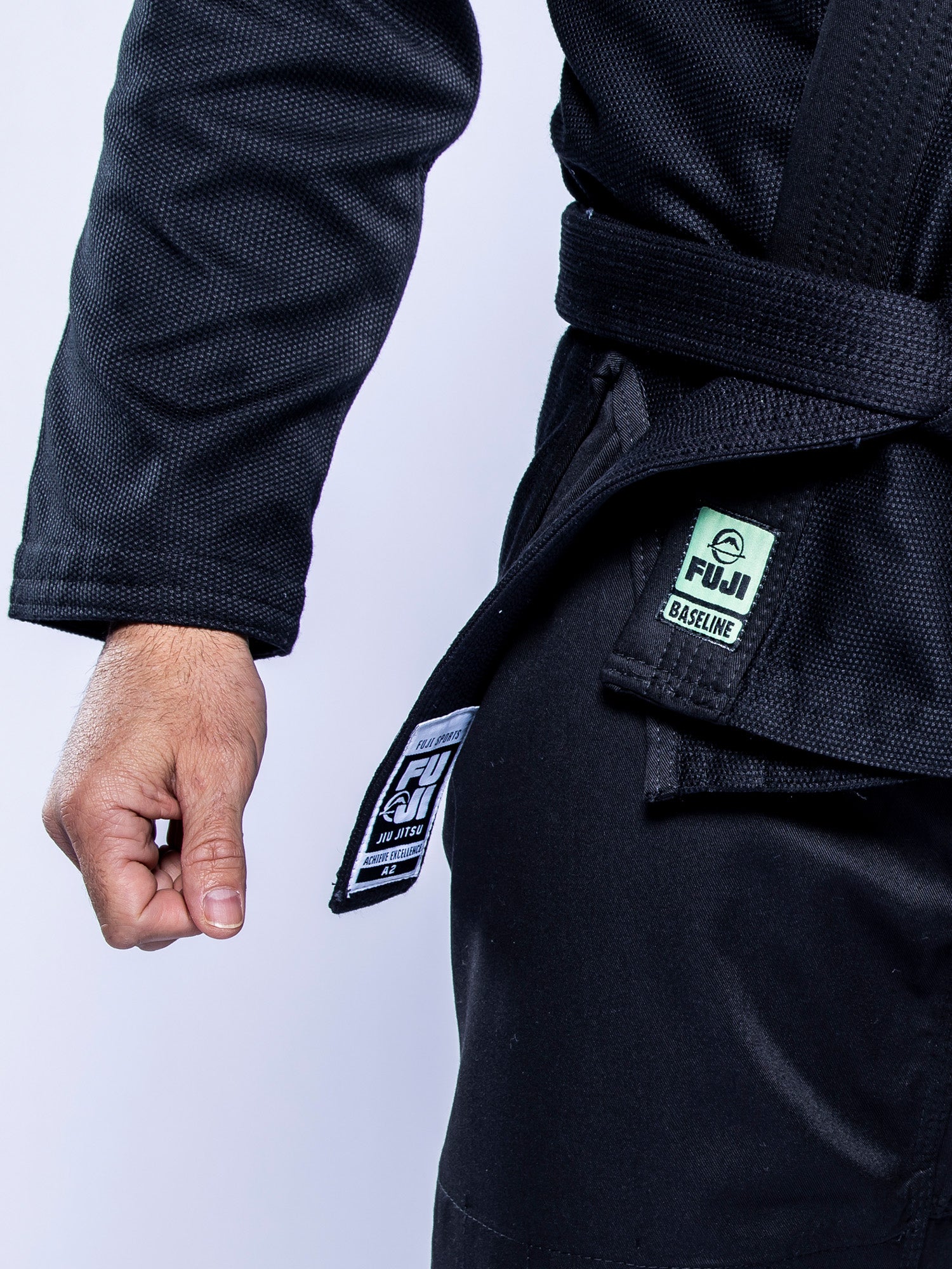 Close-up of a person wearing the Baseline 2.0 BJJ Gi Black Mint, displaying their right arm and clenched fist by their side. The gi belt is tied, and only part of the upper body is visible.