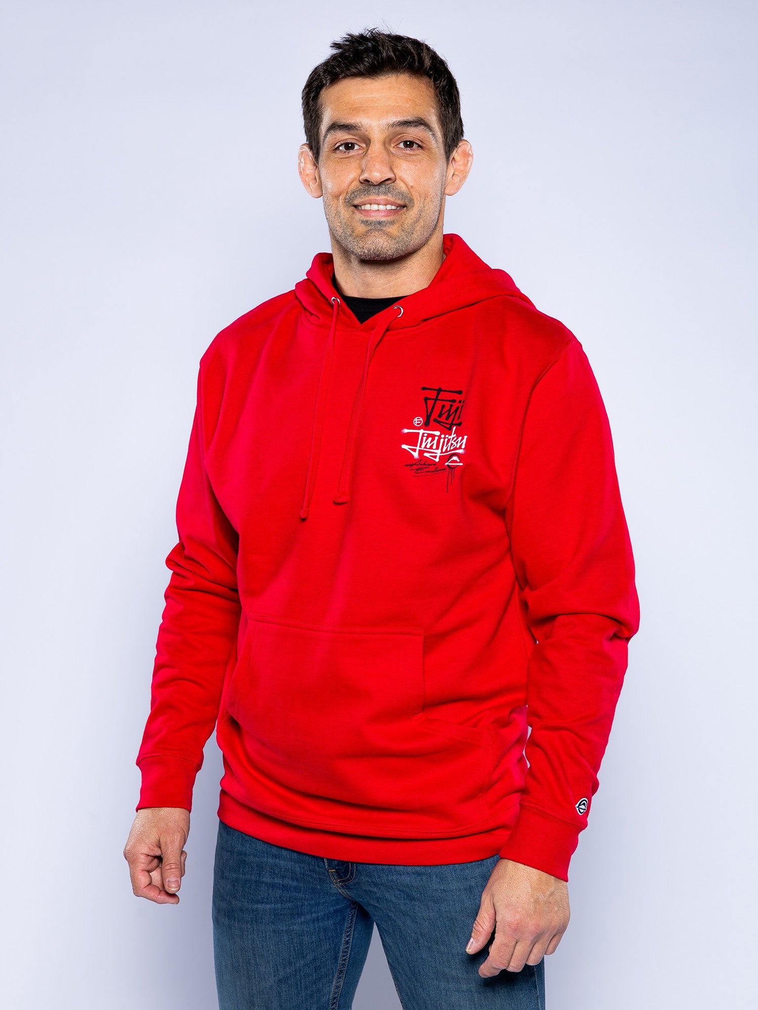 A man smiles, wearing the Japanese Street Art Hoodie Red featuring a small white chest graphic and blue jeans, posed before a plain light gray background.