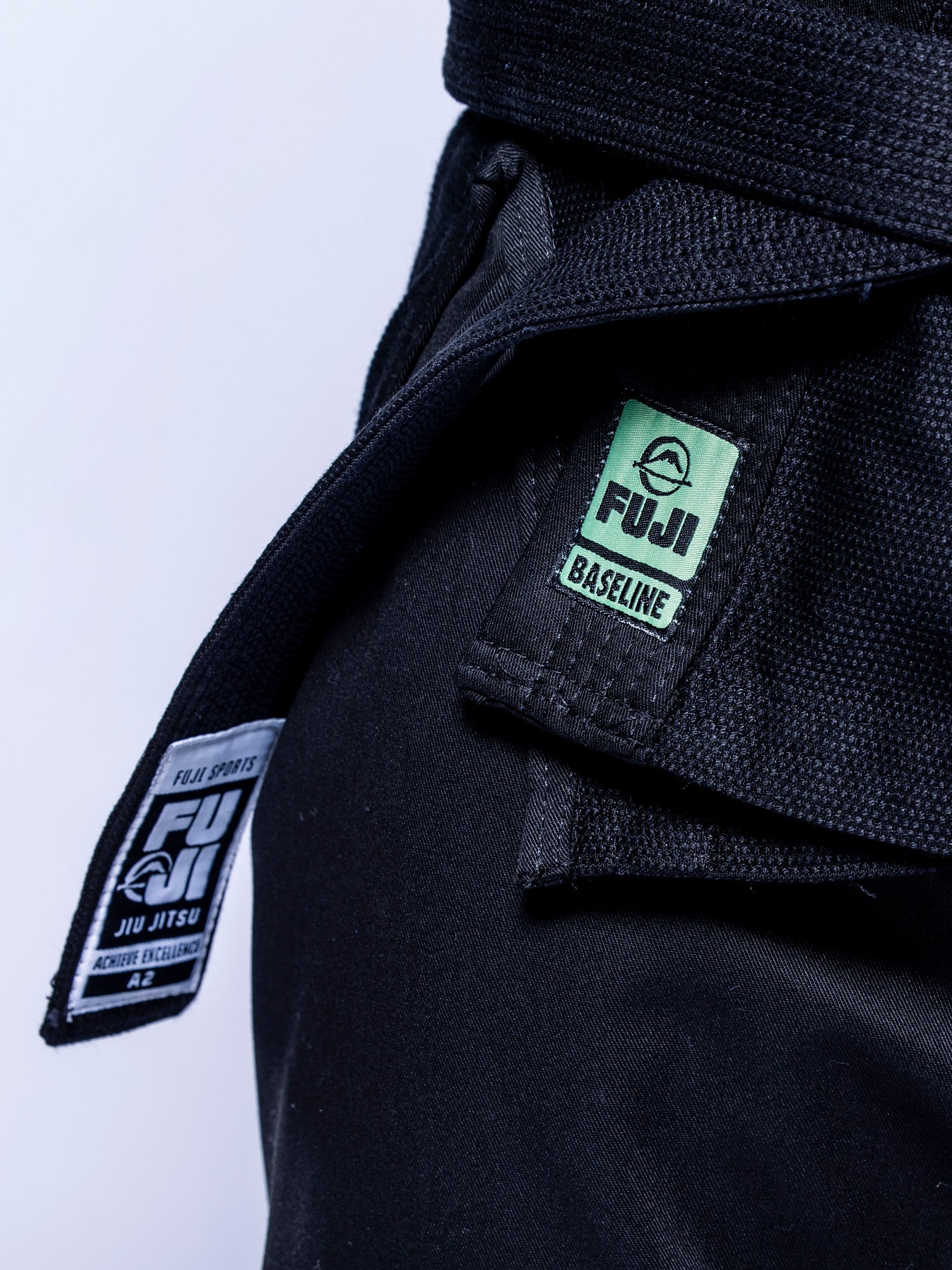 Close-up of the Baseline 2.0 BJJ Gi Black Mint with a tied black belt, featuring a green FUJI Baseline patch and a black-and-white FUJI Sports Jiu Jitsu tag.