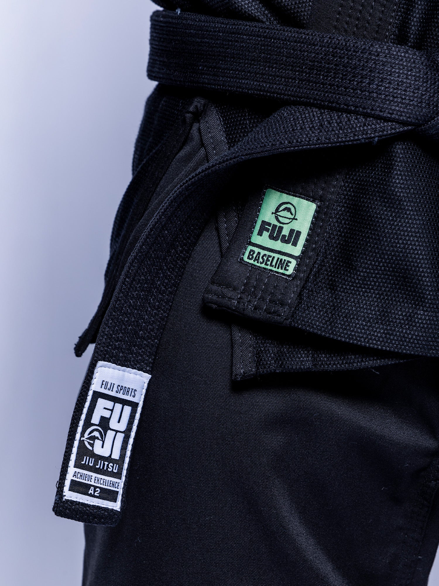 Close-up of a person wearing the Baseline 2.0 BJJ Gi Black Mint with a black belt. Visible labels read FUJI BASELINE and FUJI SPORTS JIU JITSU ACTIVE EXCELLENCE A2.