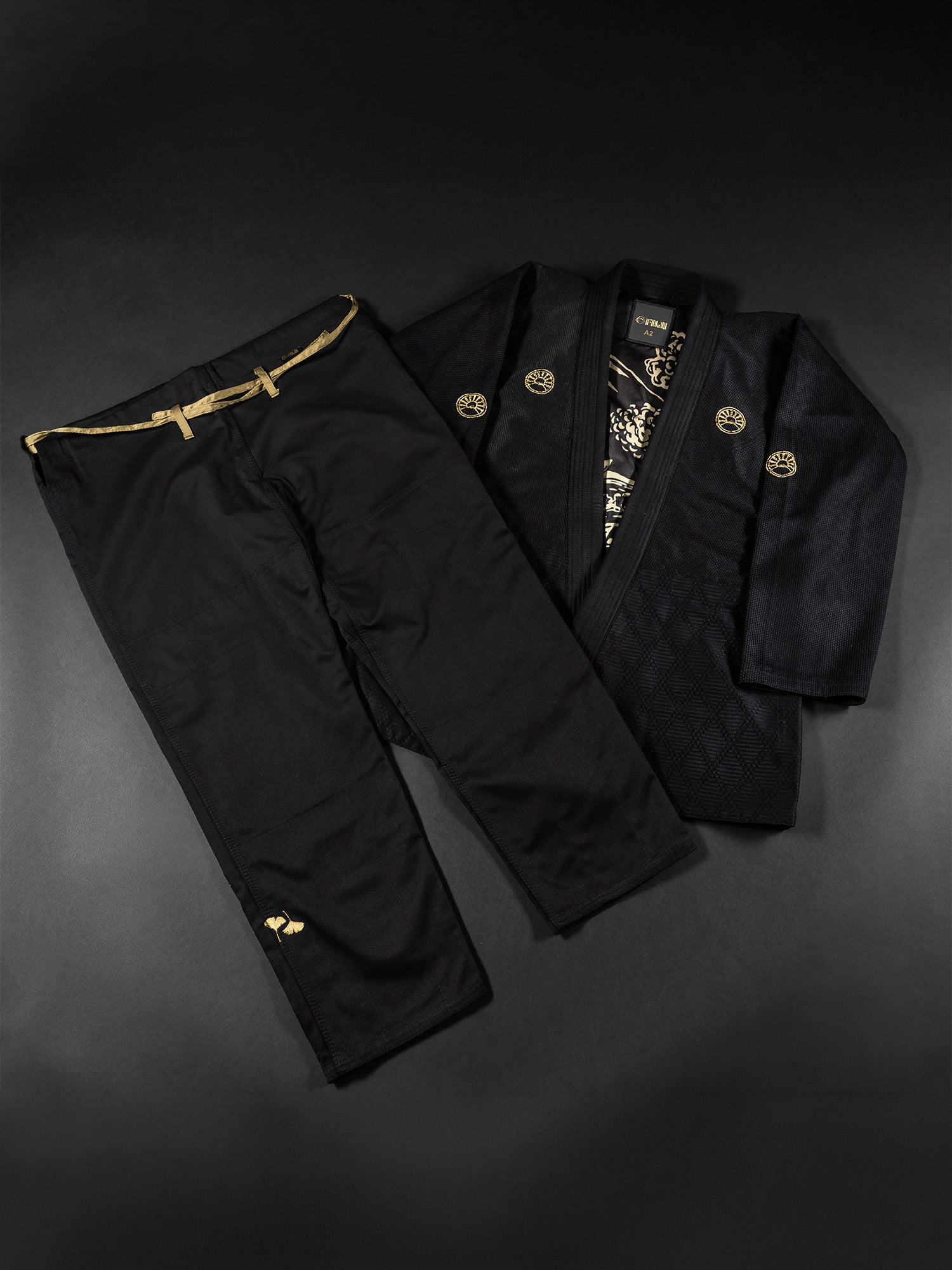 The Heritage Keishō Edition Bundle, featuring black pants with a slim gold belt paired alongside a black kimono-style jacket adorned with gold emblems, is displayed on a dark background.