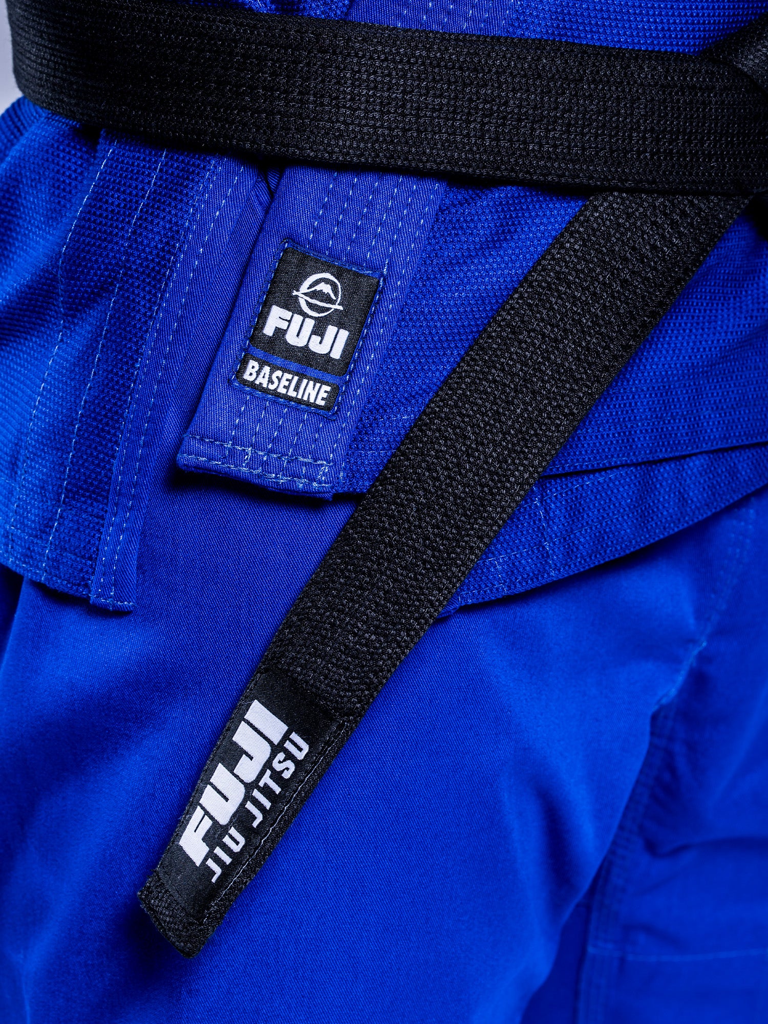 Close-up of the Baseline 2.0 BJJ Gi Blue White with a black belt tied around the waist, both featuring FUJI labels in white text and a small icon.