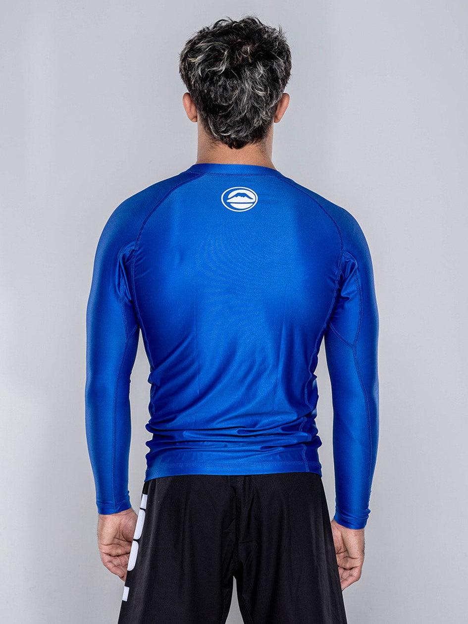 A man stands with his back to the camera, wearing the Baseline 2.0 Long Sleeve Rashguard in navy and black shorts, set against a plain light gray background.