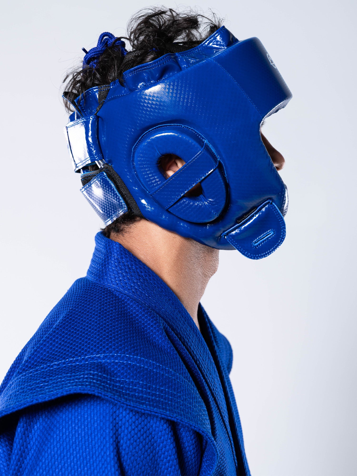 A person wearing a blue martial arts uniform and the FIAS Sambo Combat Headgear Blue, shown in profile against a plain background.