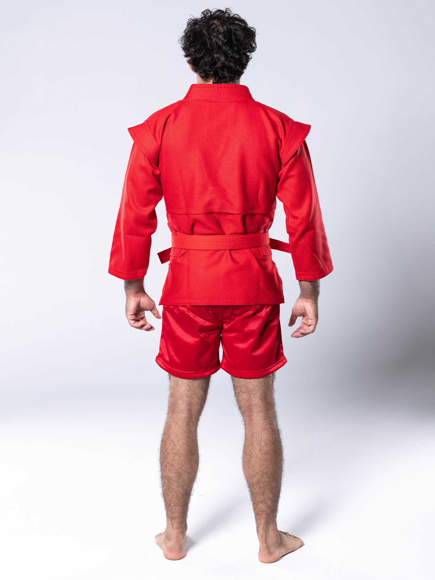 A person stands barefoot facing away, wearing the FIAS Sambo Kurtka Jacket Red with Red Belt and matching shorts against a plain white background.
