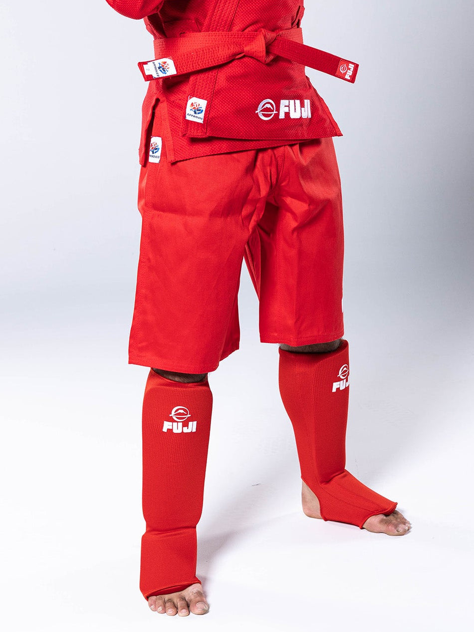 A person wearing FIAS Combat Sambo Shorts Red, a matching jacket with a belt, and shin guards.